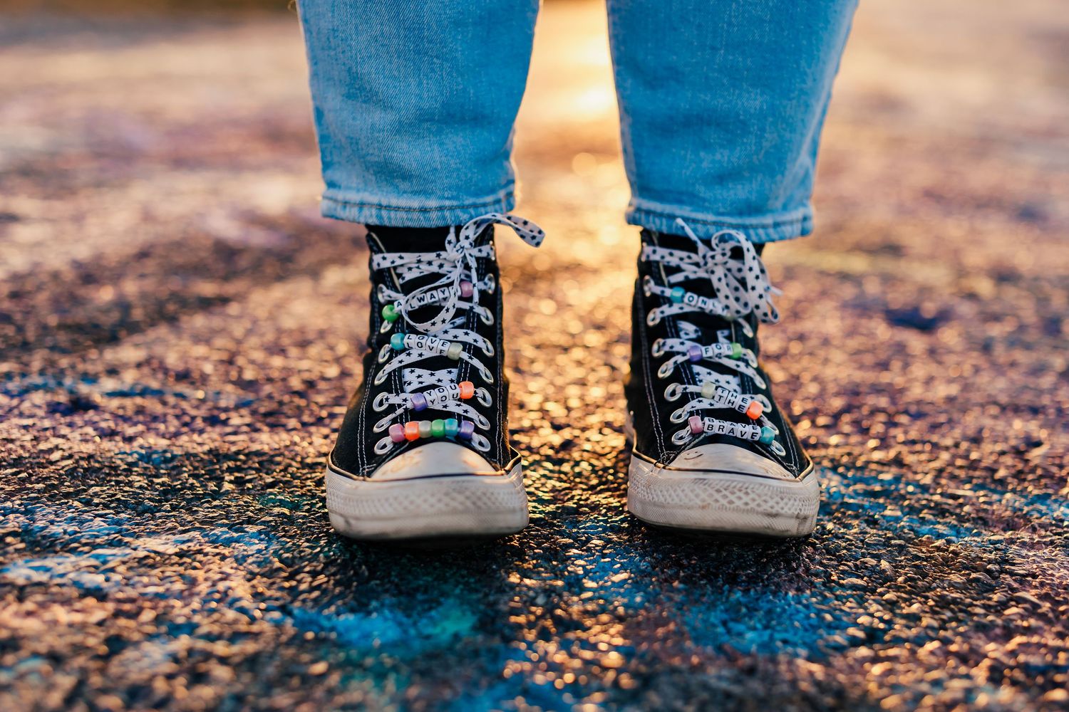 Close-up view of blue jeans and gray sneakers on textured ground.