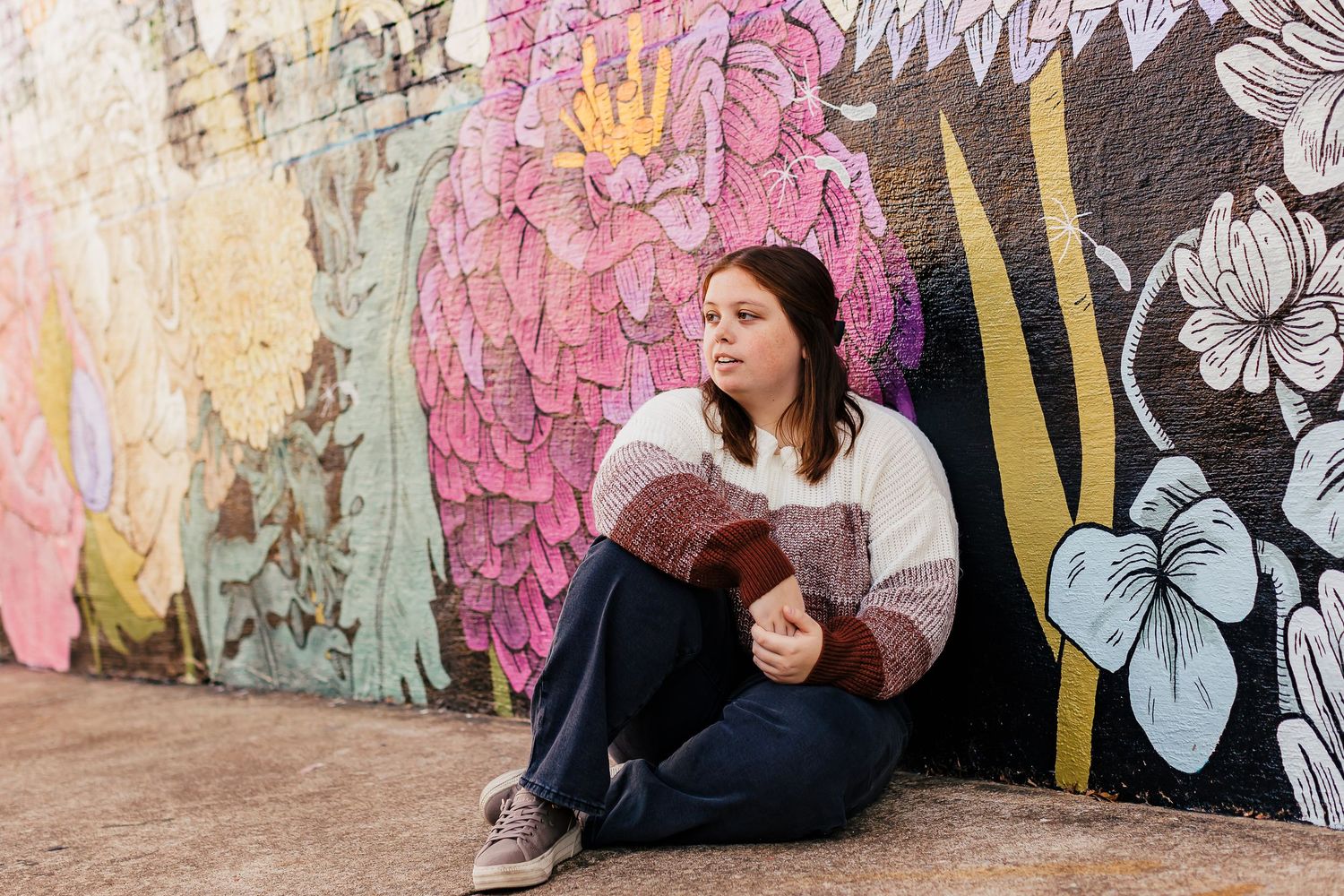 A person sits against a wall decorated with vibrant pink and floral street art.