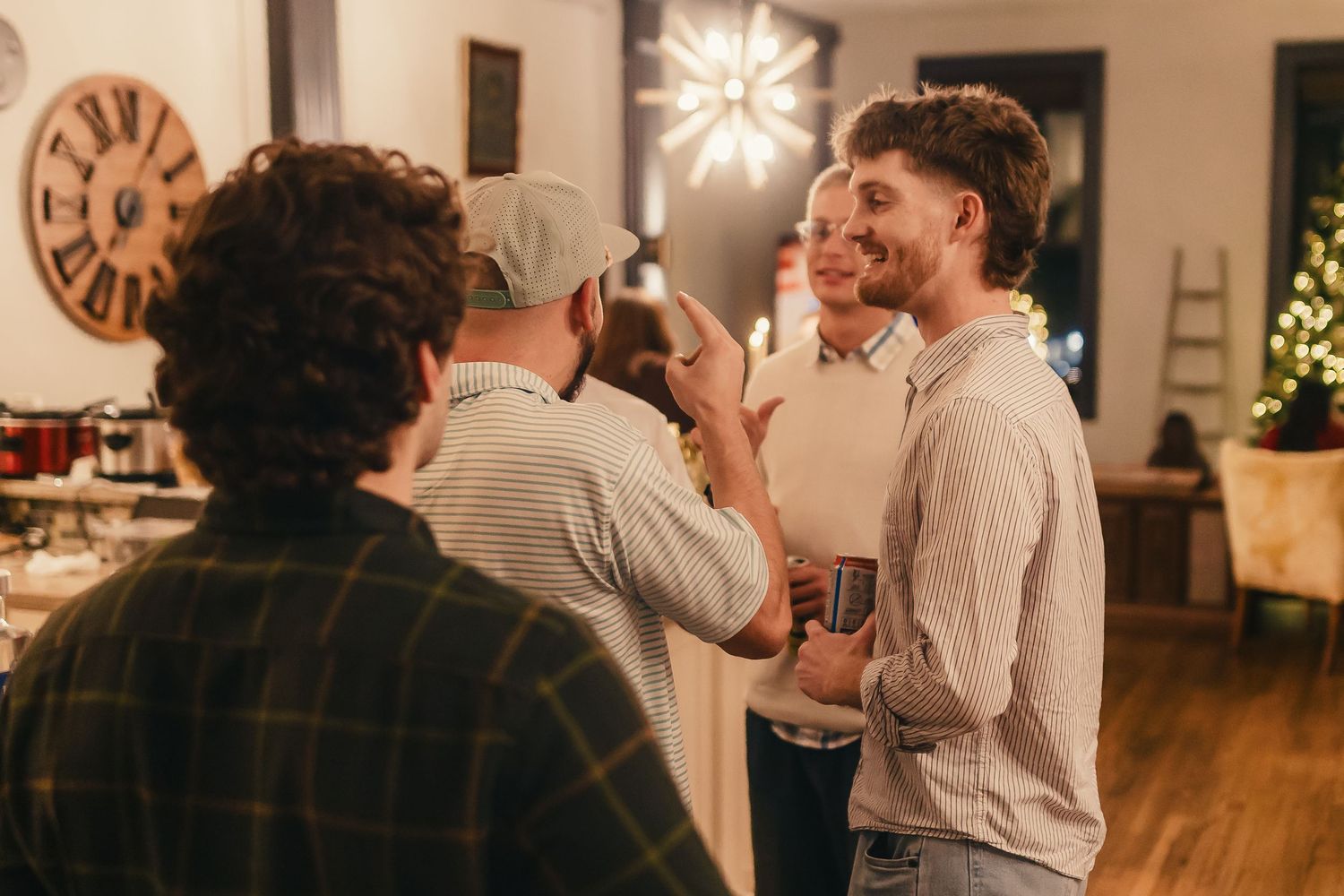People socializing at an indoor gathering with decorative lighting and wooden furniture visible in the background.