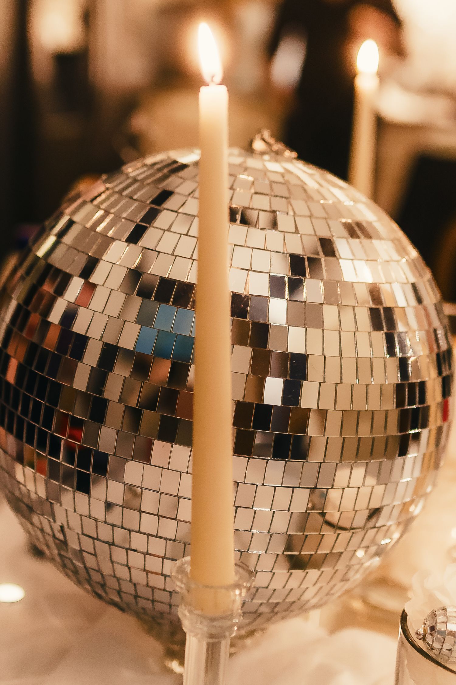 Shiny disco ball with mirror tiles reflects warm candlelight creating a festive party atmosphere.