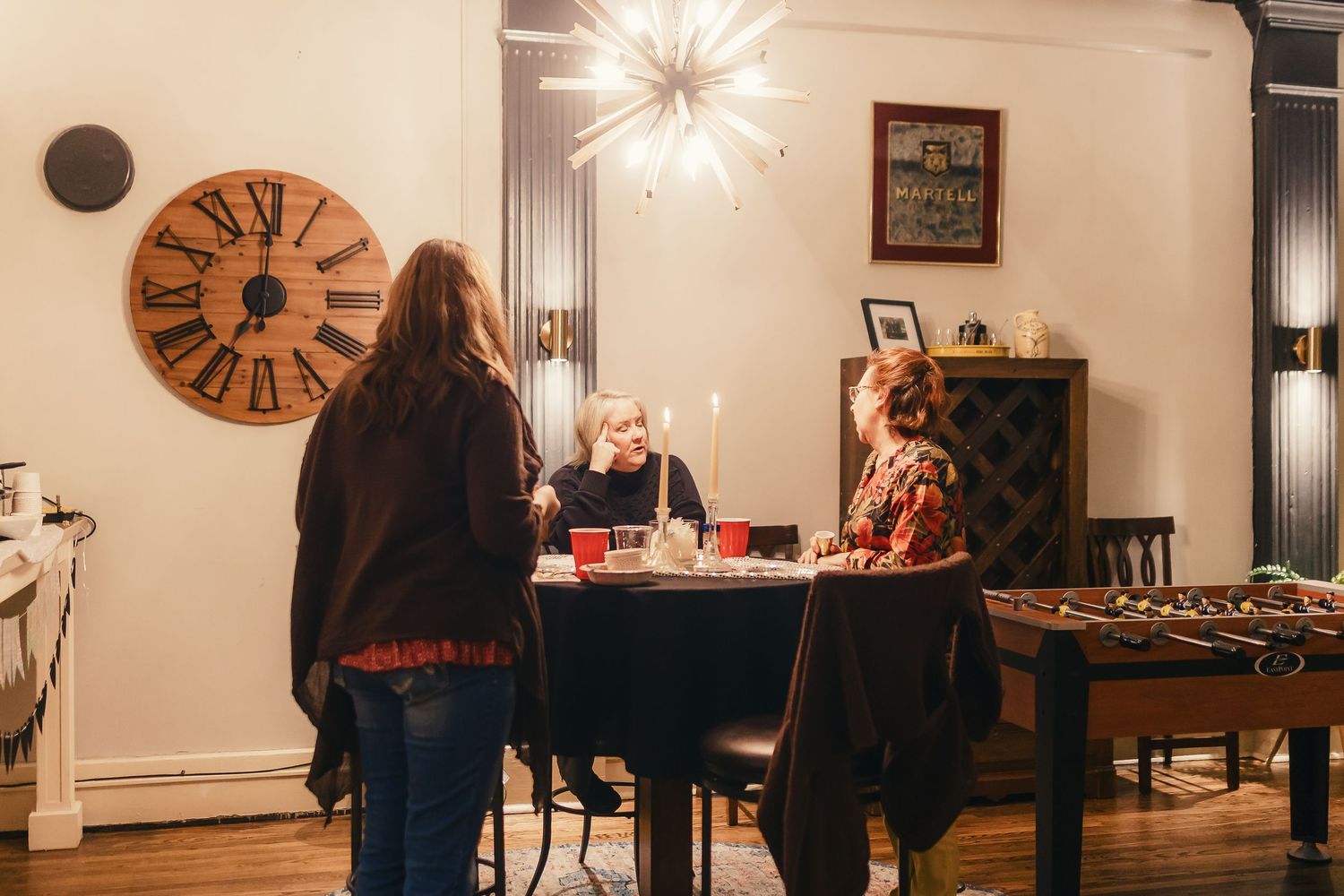 A cozy dining room with vintage decor features a large wall clock and modern chandelier lighting.