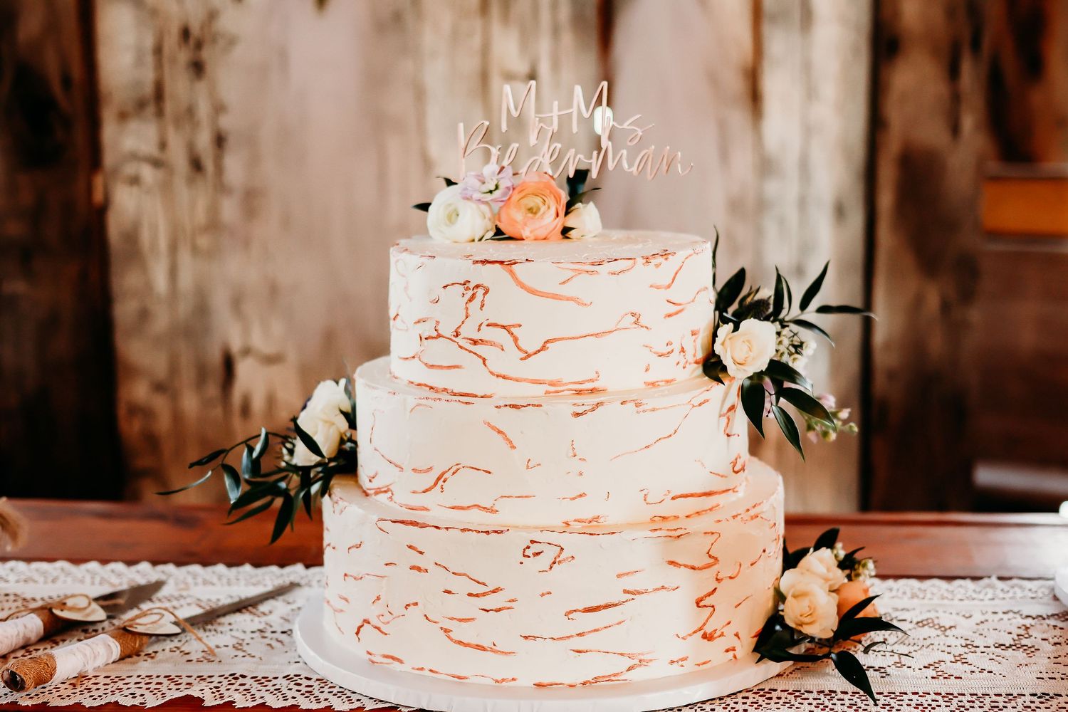 Three-tiered white wedding cake with delicate coral-colored swirl details and fresh floral accents.