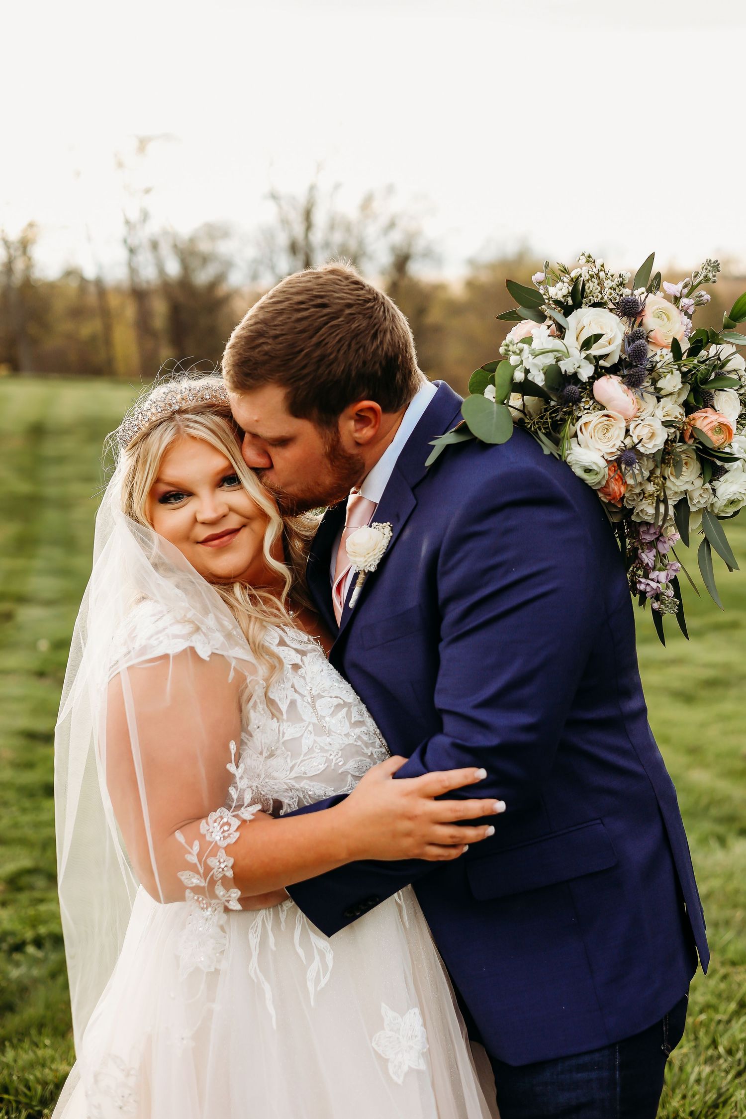 A romantic outdoor wedding moment with a bouquet of white and peach flowers.