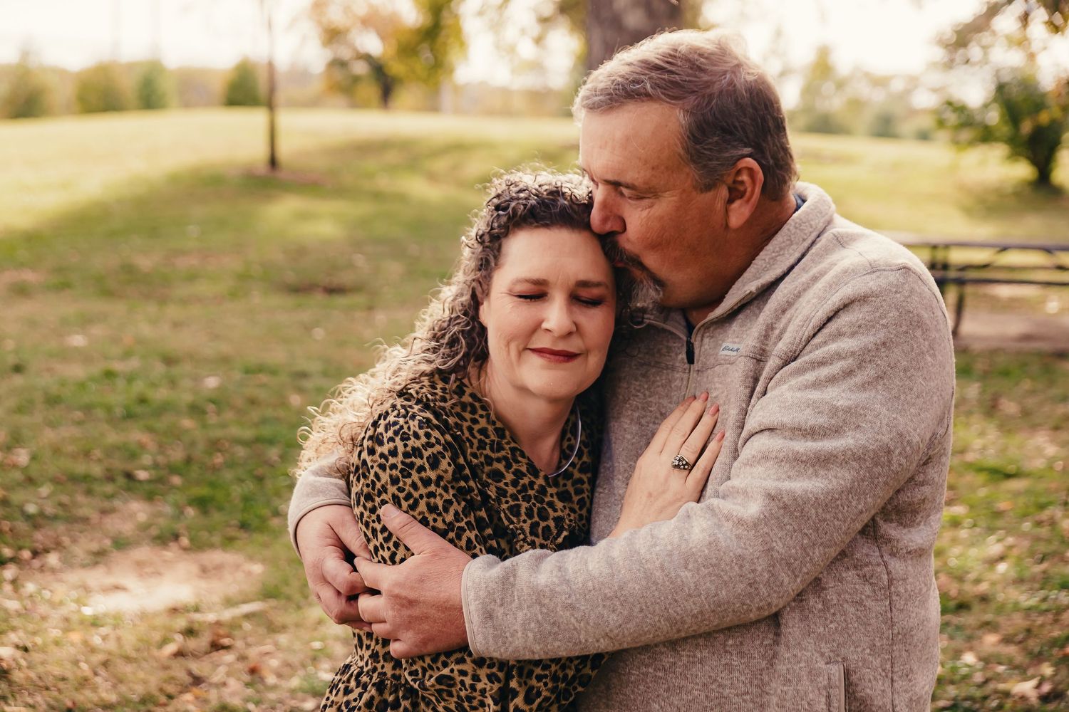 A tender embrace captured between two people during golden hour in a pastoral setting.