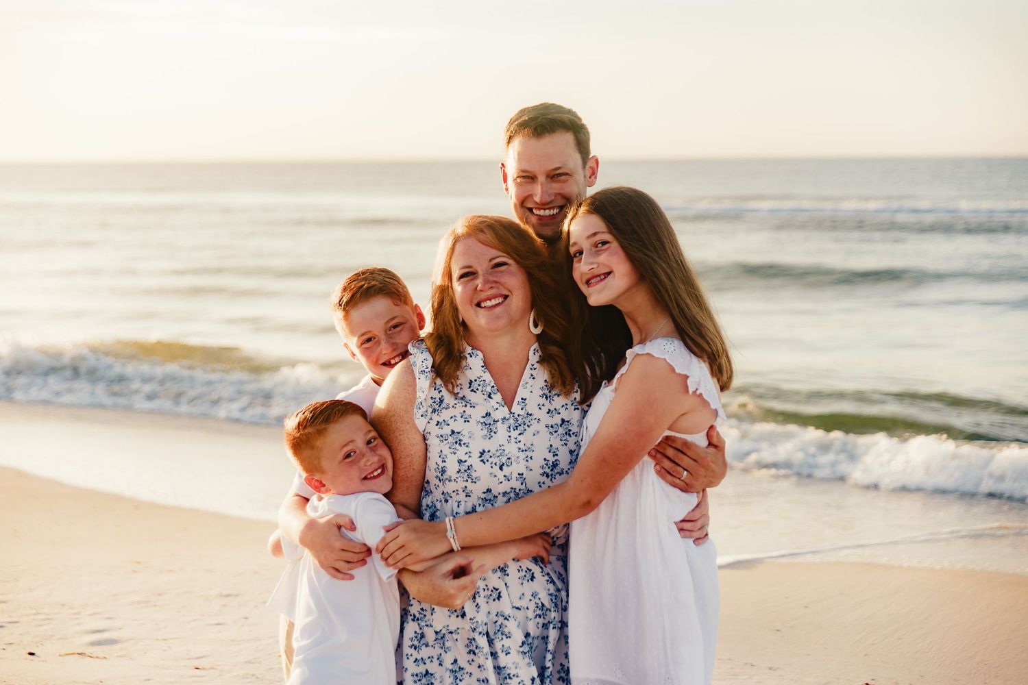 Happy family embraces while standing together on beach during golden hour photo session.