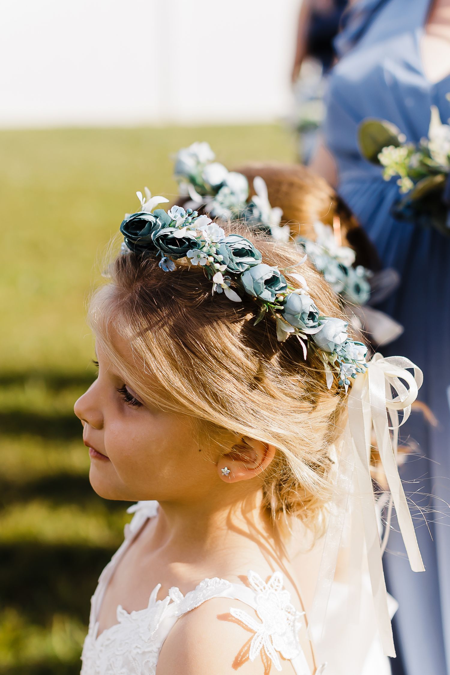 A delicate floral crown adorns a young attendant's hair in soft sunlight.