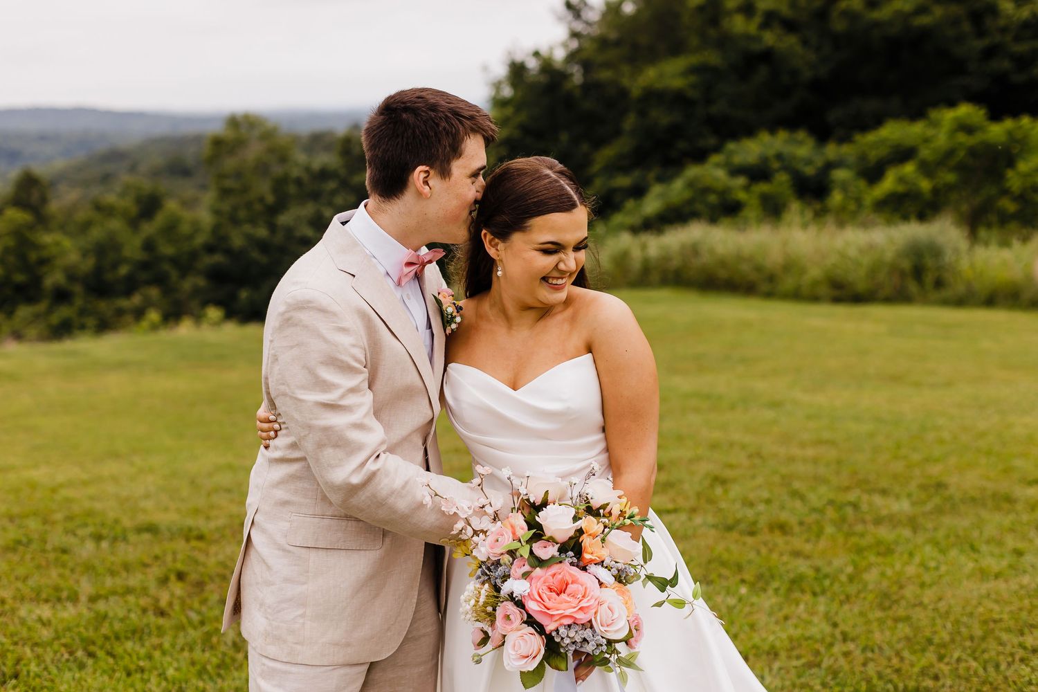 A romantic wedding portrait captured in a sunlit mountain meadow with pink bouquet.
