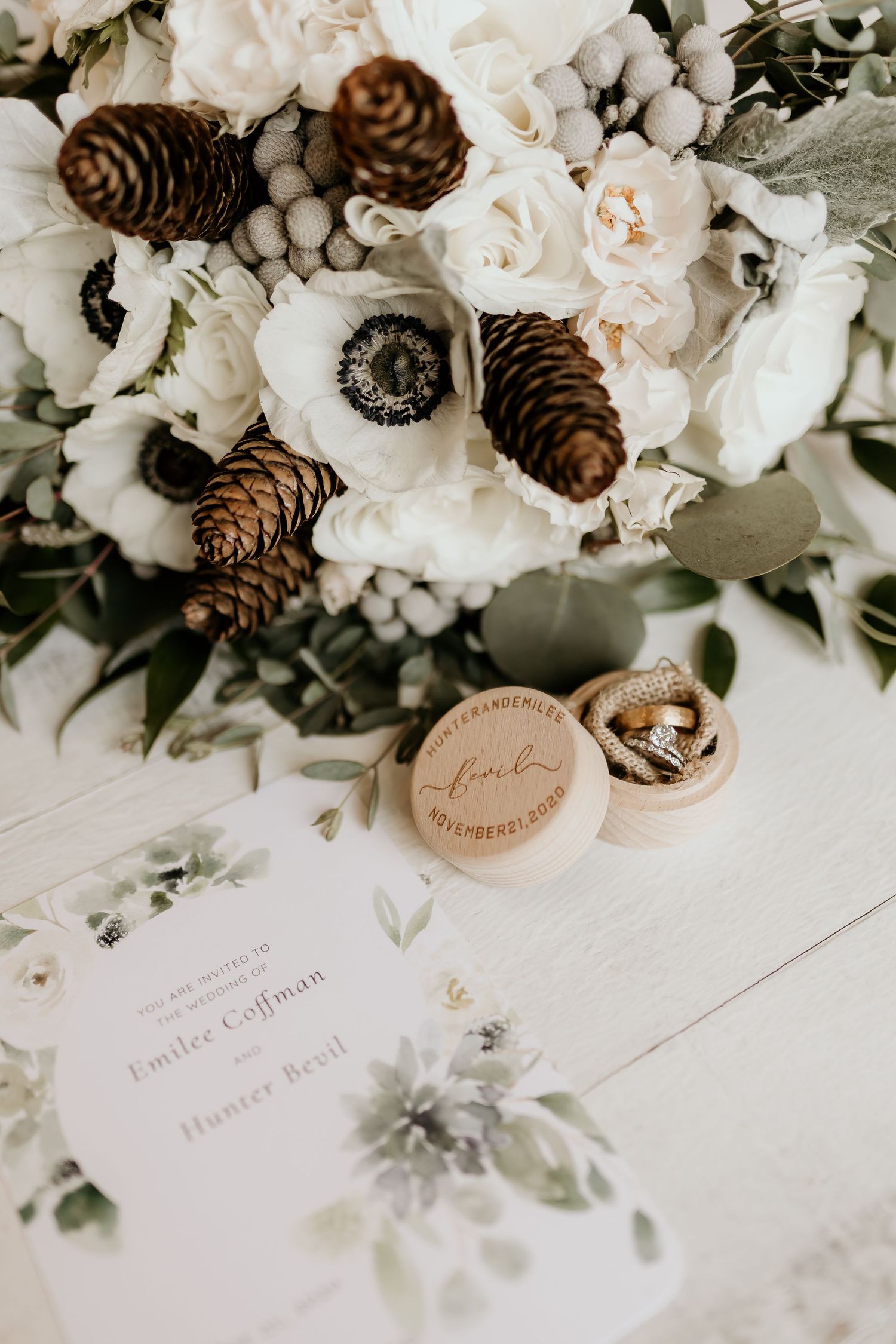 Wedding stationery and decor featuring white flowers, pinecones, and elegant calligraphy on white paper.