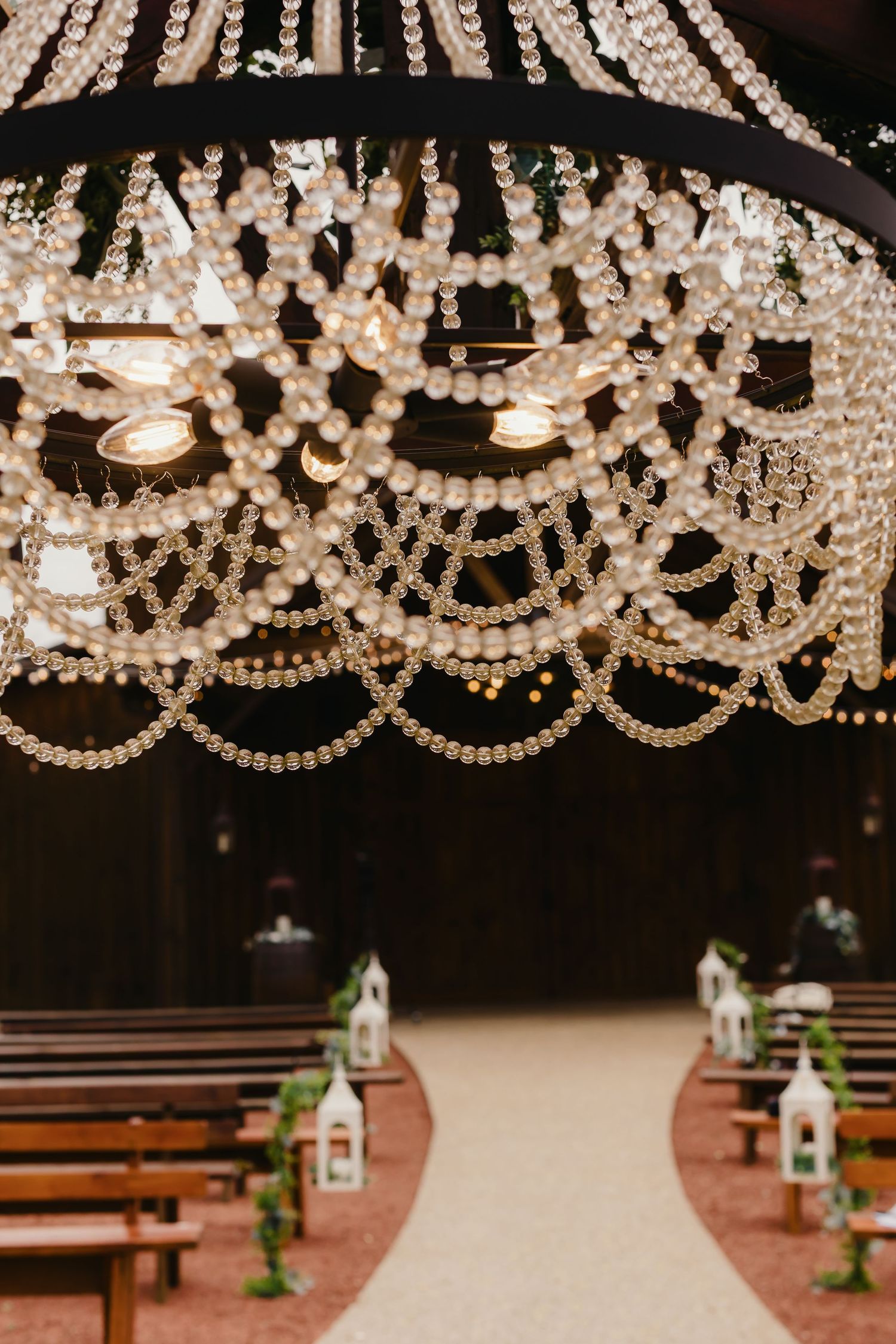 Elegant crystal chandelier hanging over wooden church pews at wedding venue.