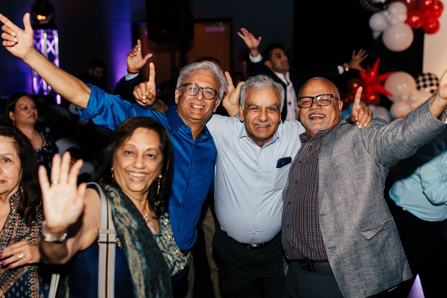 A group of people celebrating at a party with raised arms and joyful expressions in a dark venue with blue lighting.