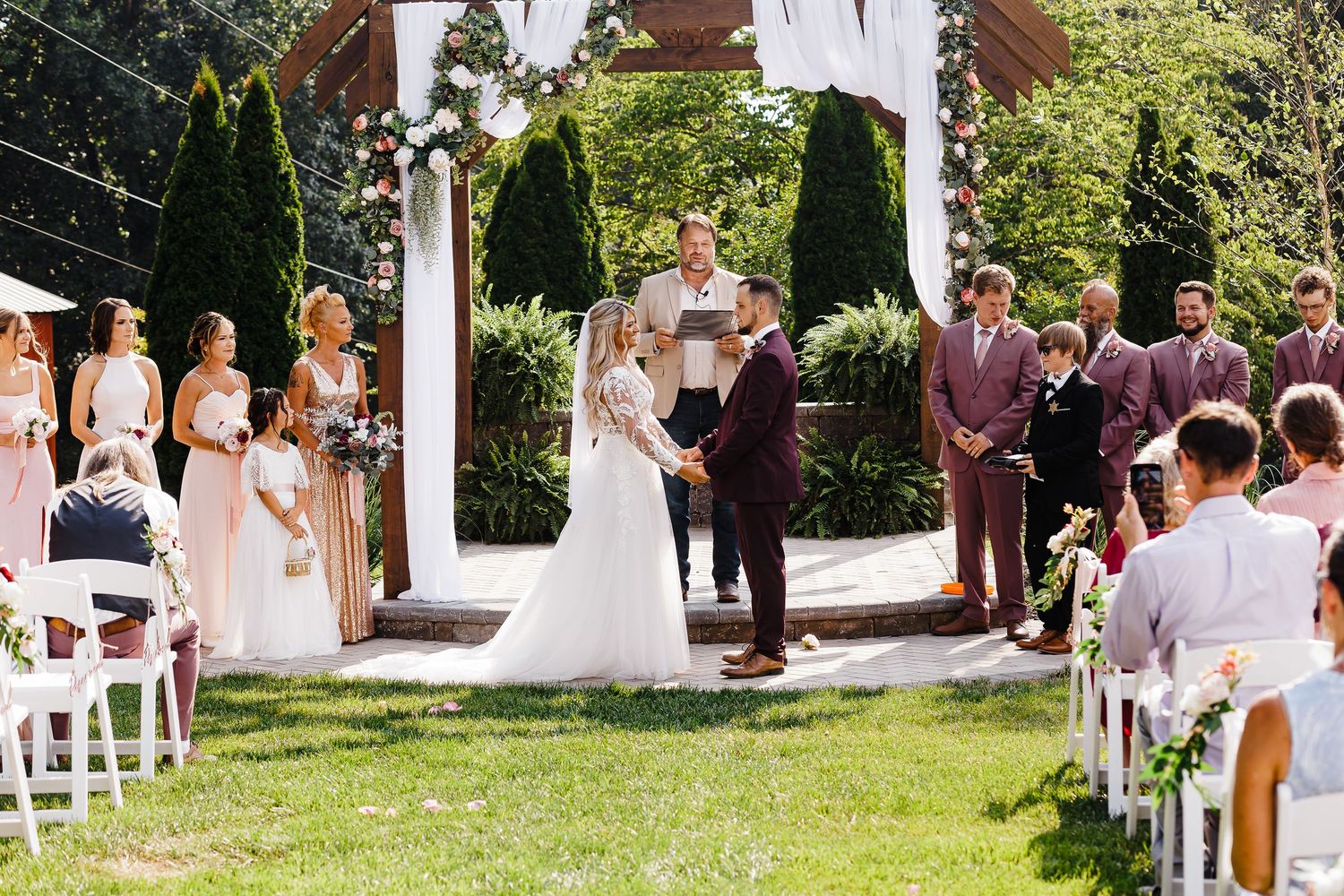 Outdoor garden wedding ceremony setup with white chairs and floral decorations.