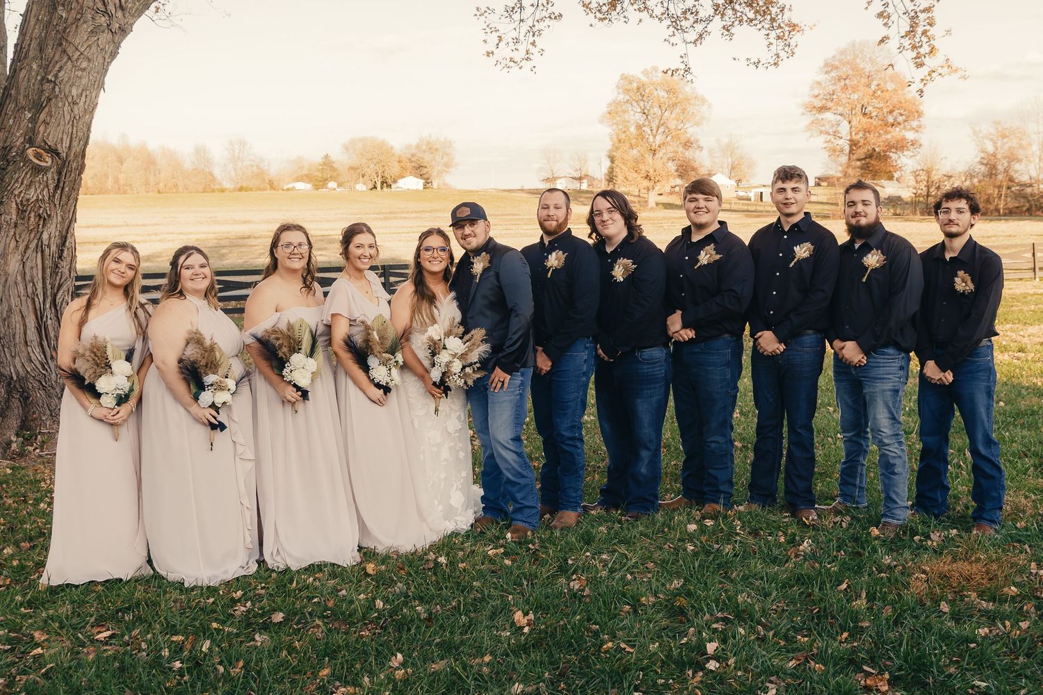 Wedding party in navy and beige attire posing together under autumn trees.