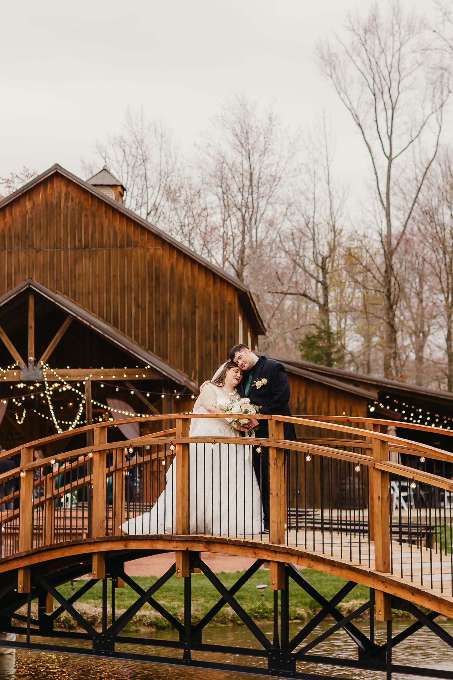 Rustic wooden barn with string lights and wooden bridge creates romantic wedding setting.