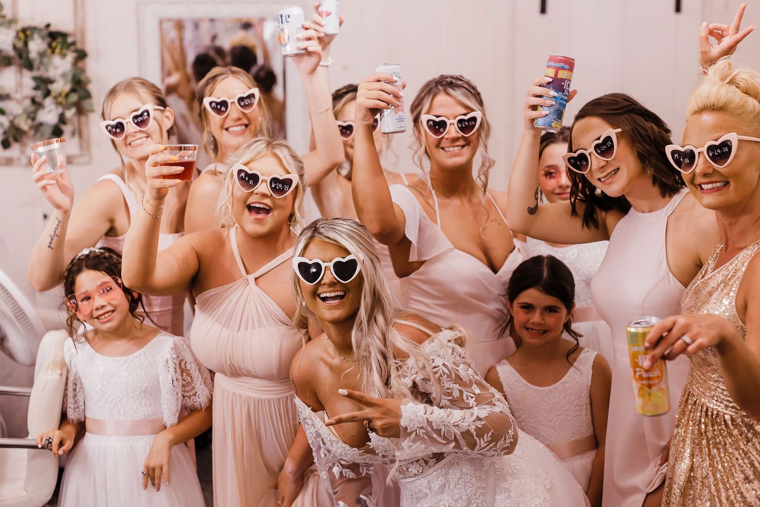 A group wearing sunglasses and light colored outfits celebrates together at a party with drinks and festive energy.