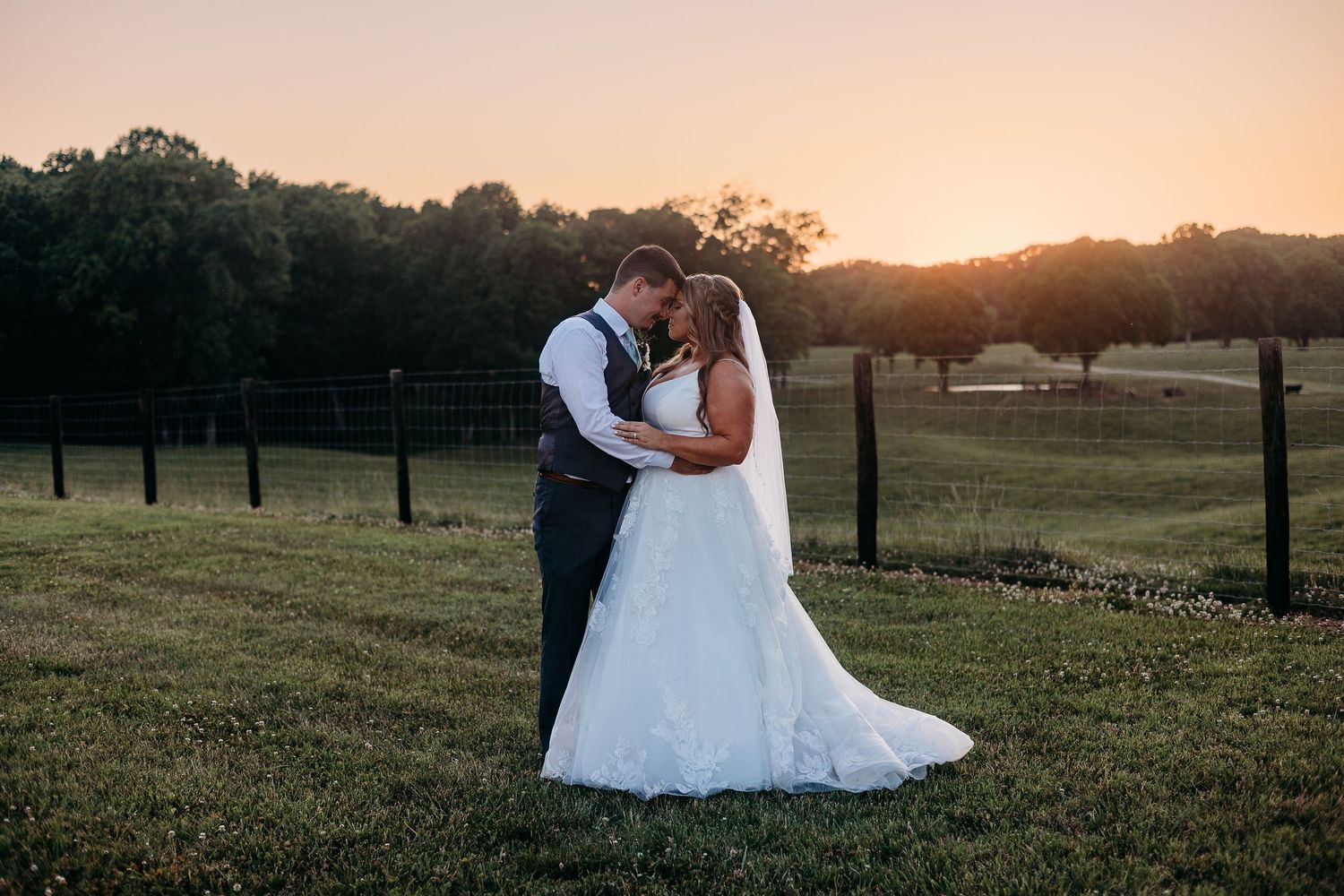 Wedding couple silhouetted against a sunset sky in an open field.