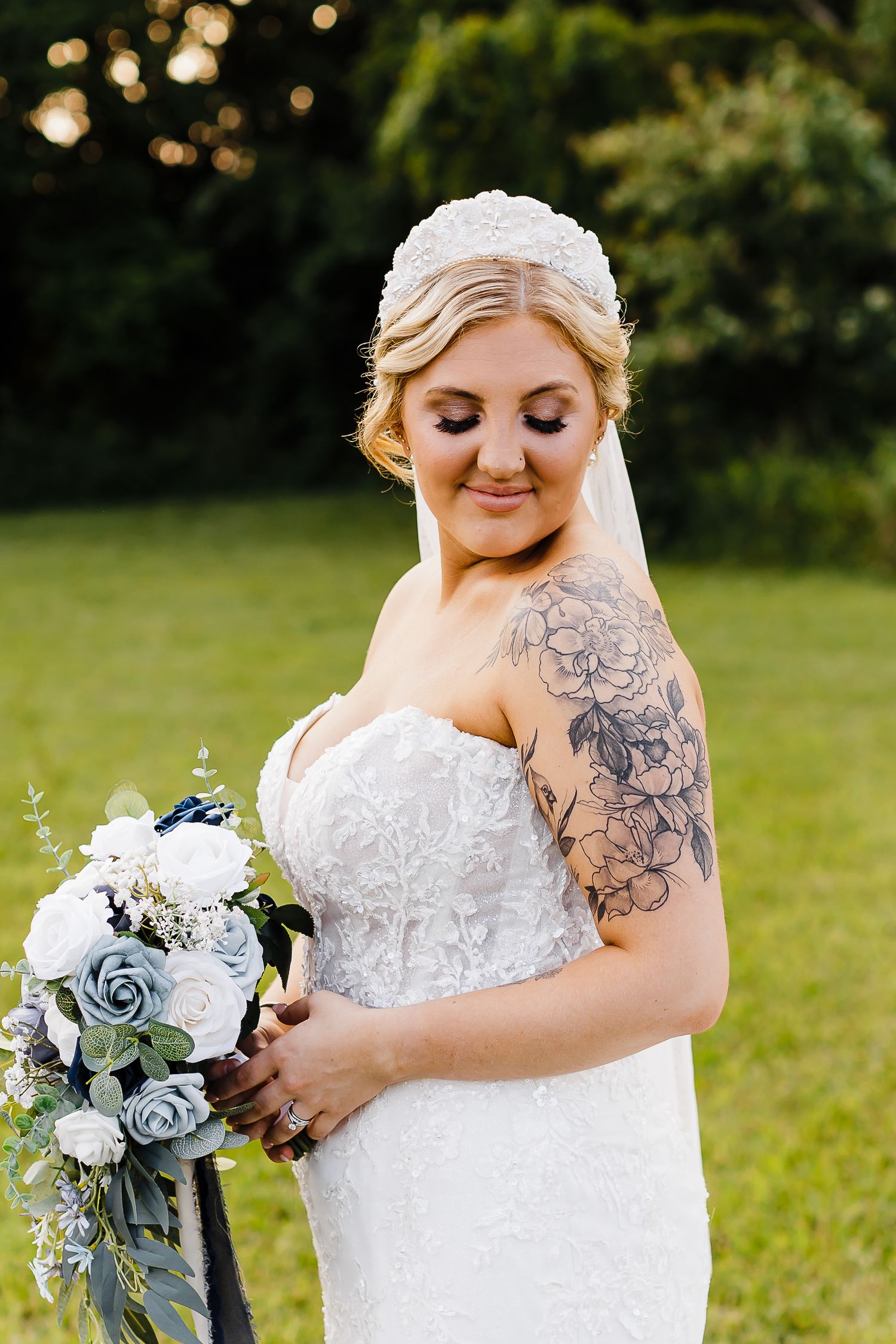 Bride in a white lace gown holds a blue and white bouquet while showing off her arm tattoo.