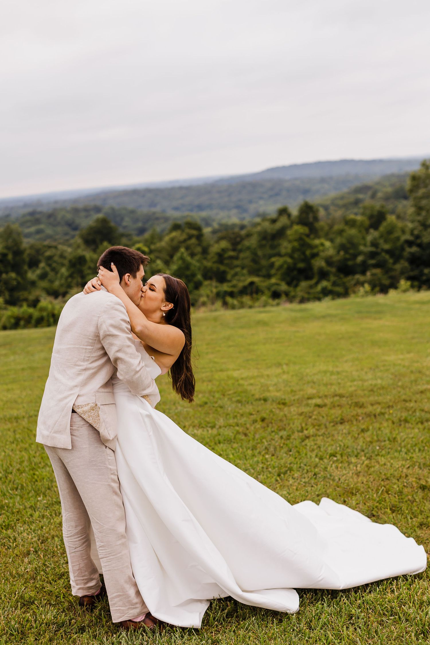 A romantic wedding kiss on a hilltop with flowing white dress and mountain backdrop.