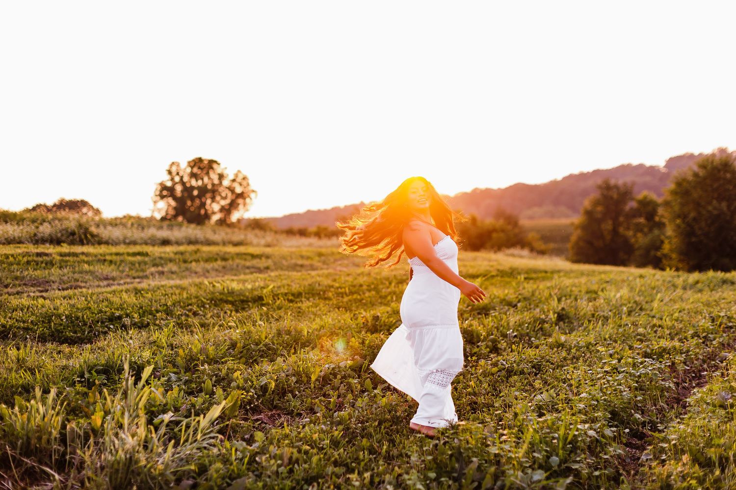 Scenic sunset landscape with figure in white clothing walking through a grassy field.