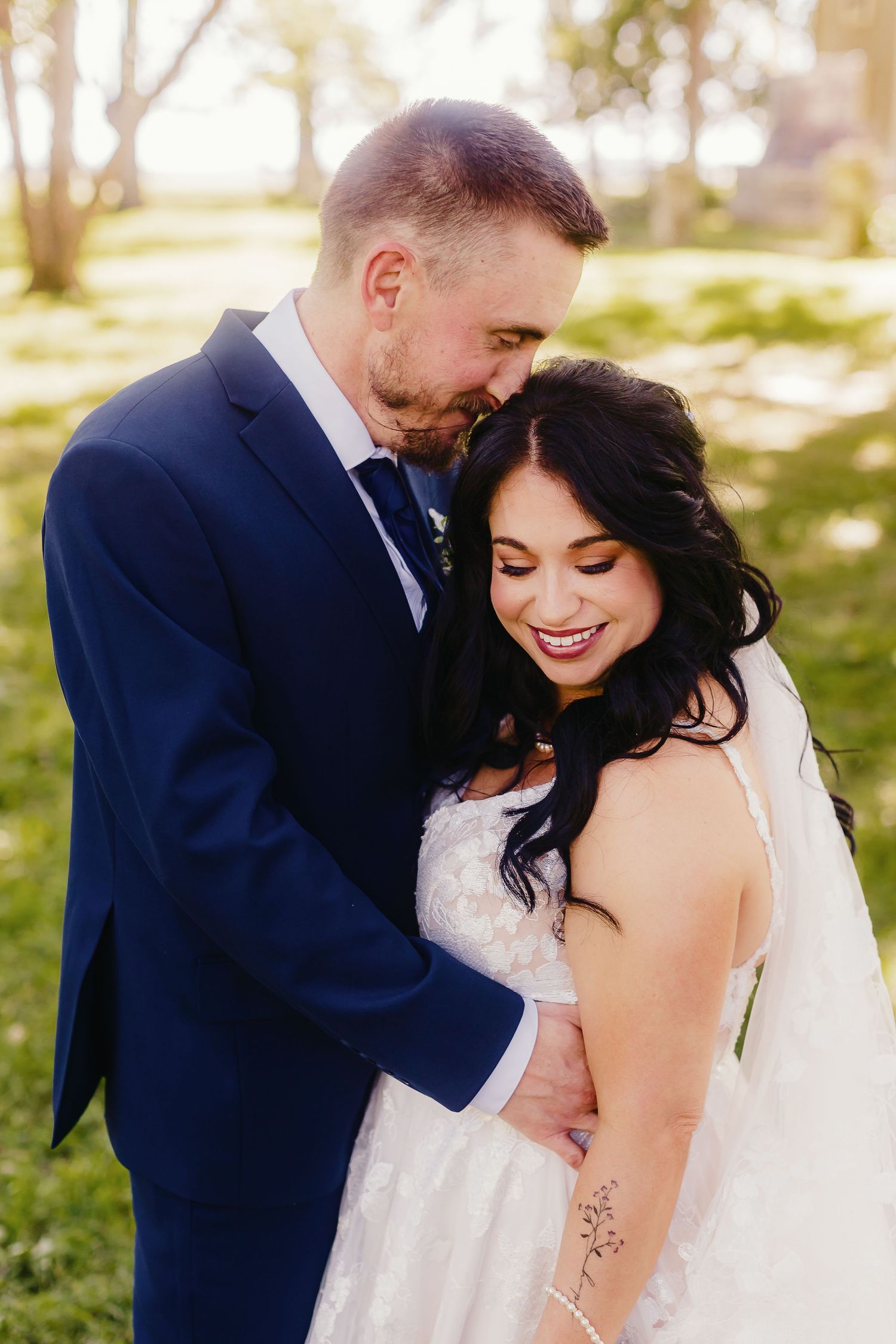 Romantic outdoor wedding portrait with couple embracing in natural sunlit setting.