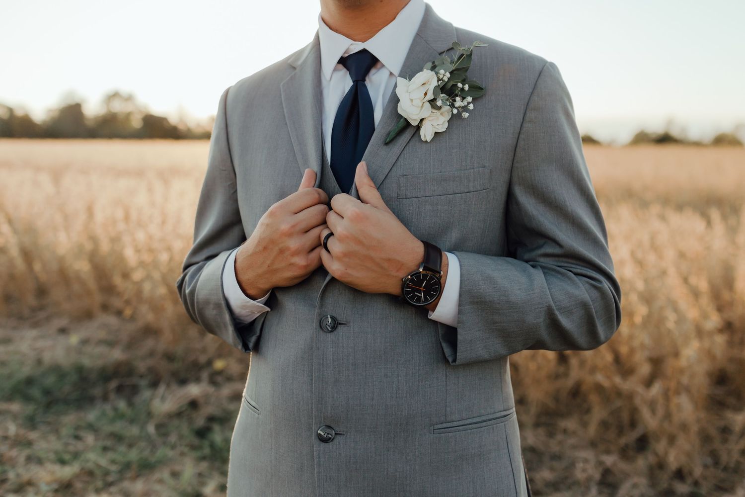 Groomsmen in grey suits with blue ties posing in a field.