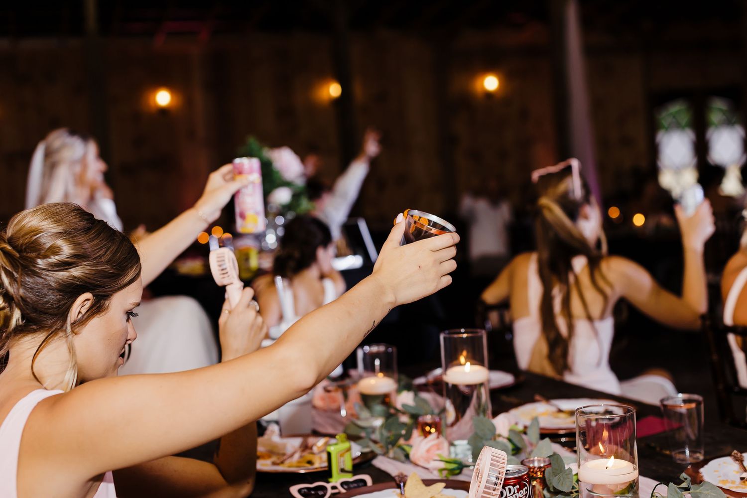 Wedding reception guests raise their glasses in a celebratory toast at a decorated dinner table.