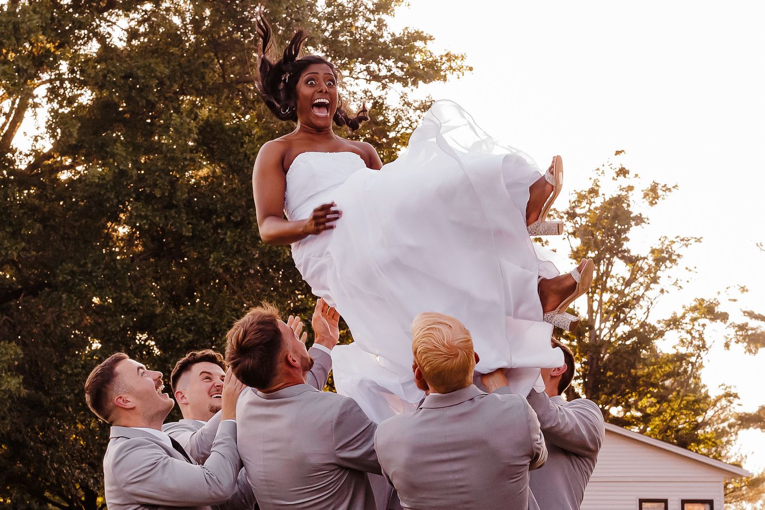 Wedding party members laugh and celebrate on a sunny lawn.