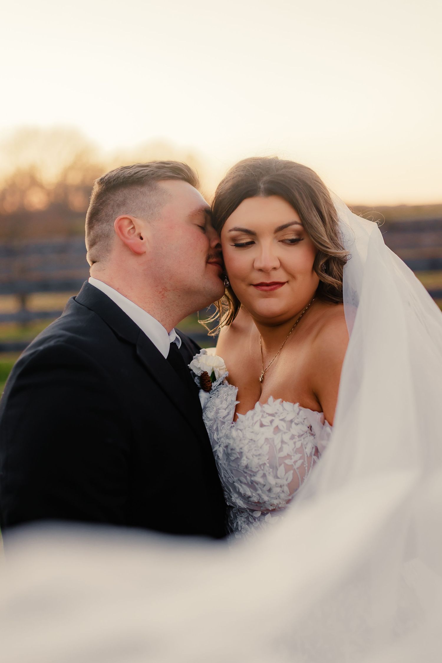 Tender moment between newlyweds captured through flowing veil at golden hour.