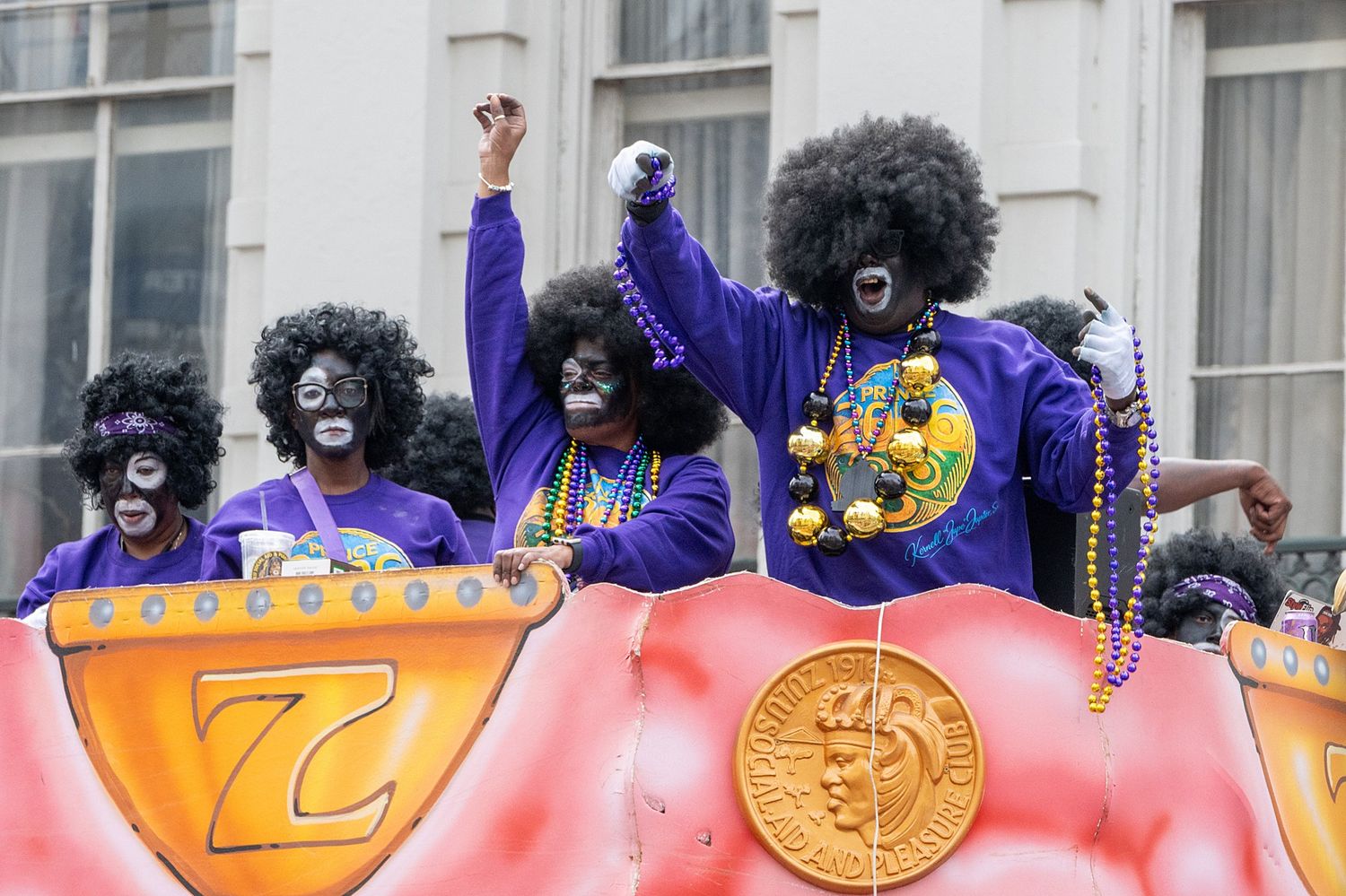 Costumed performers in purple outfits celebrating on an orange parade float.