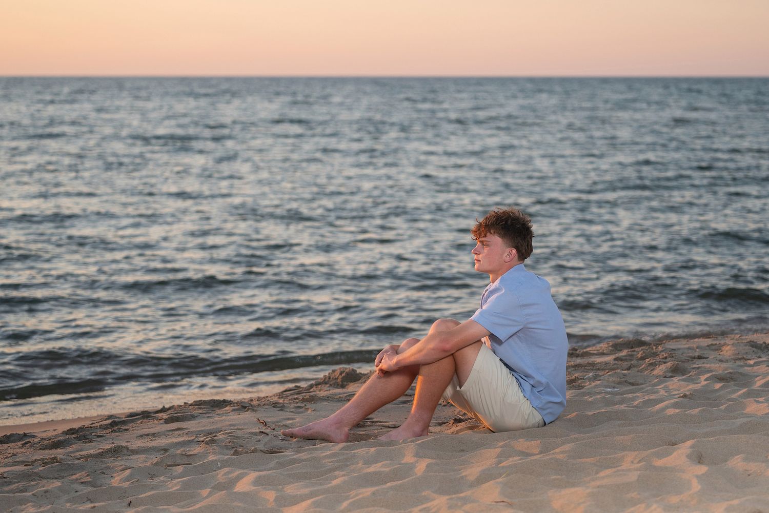 Person sitting peacefully on beach watching sunset over ocean waves.