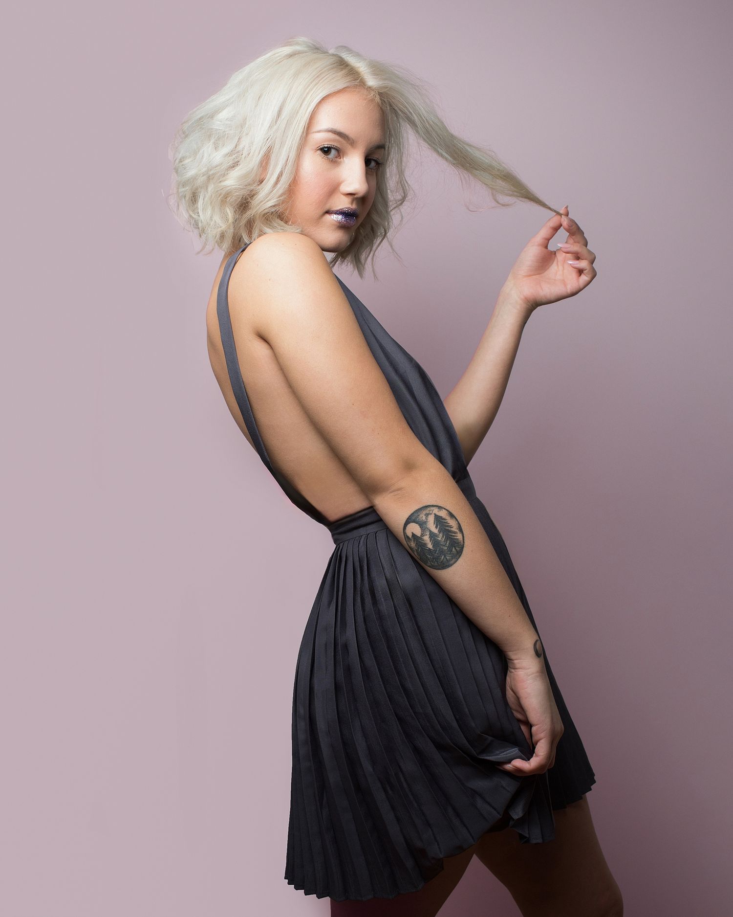 Fashion portrait of model in black dress posing against light purple background.