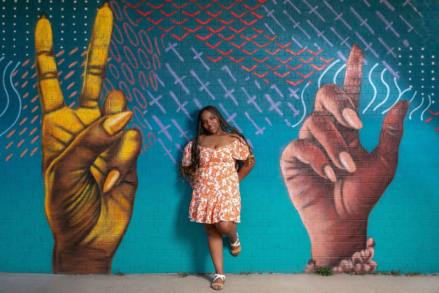 Urban portrait against vibrant turquoise wall with painted hand gestures mural.