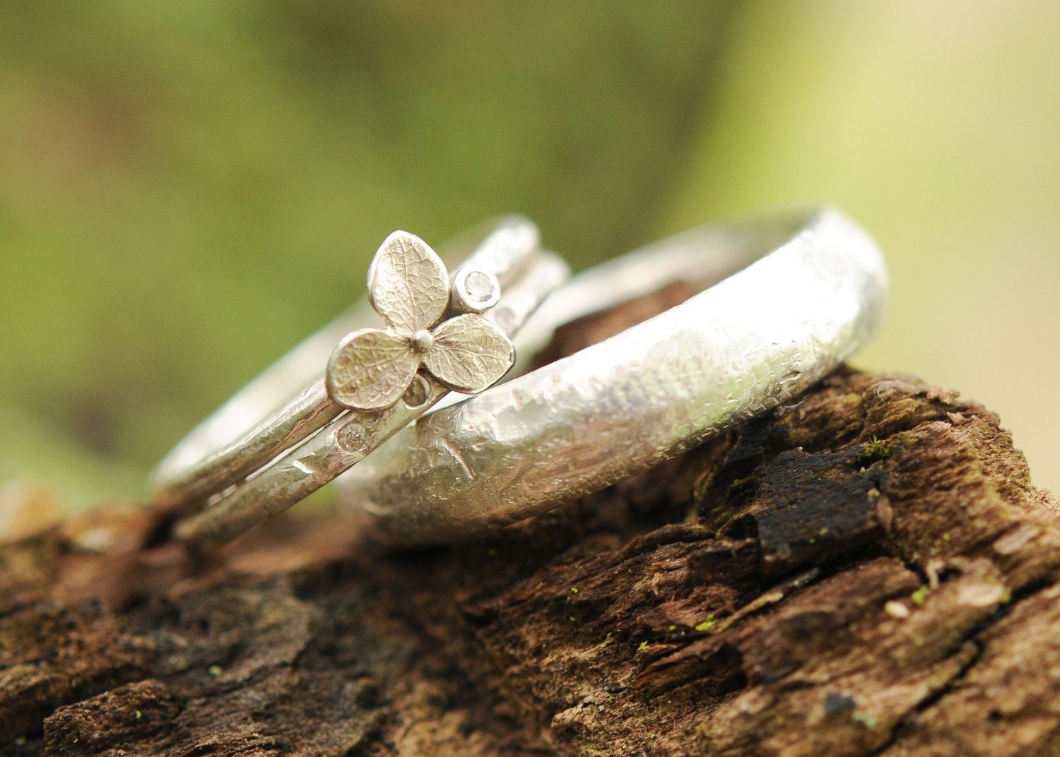 Two silver wedding rings with floral designs photographed on rustic wood.