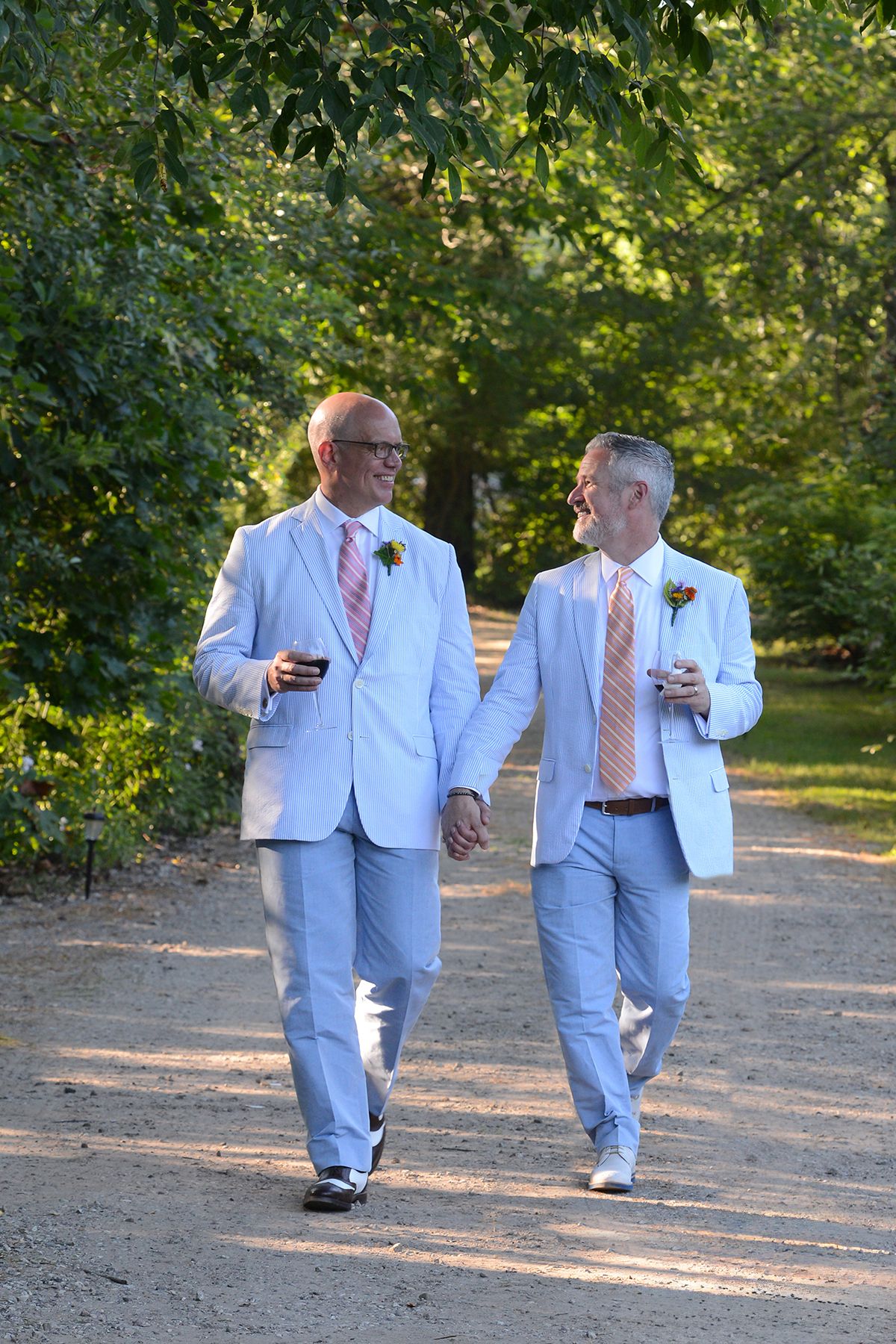 Groomsmen in light blue suits walking along garden path during wedding.