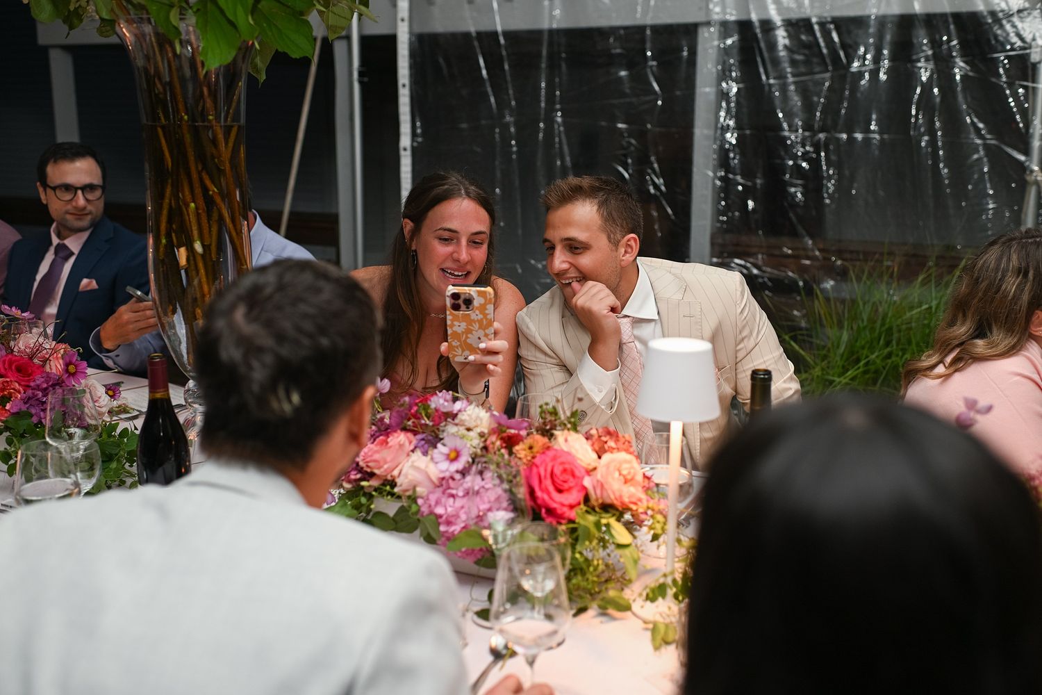 Wedding guests mingle and socialize at an elegant outdoor reception with floral centerpieces and string lights.