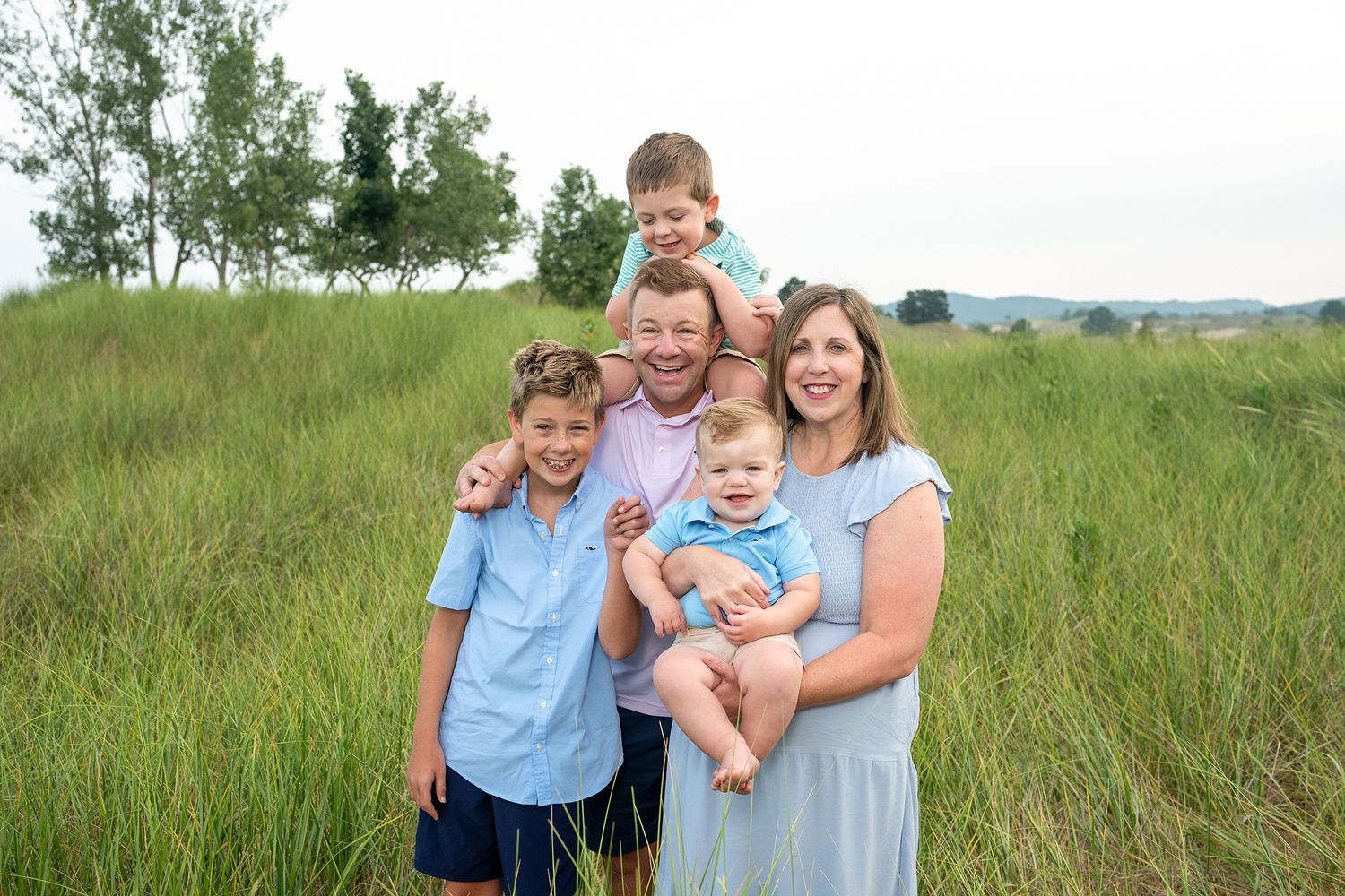 Happy family of five posing in a lush green field, parents with three young boys smiling outdoors.