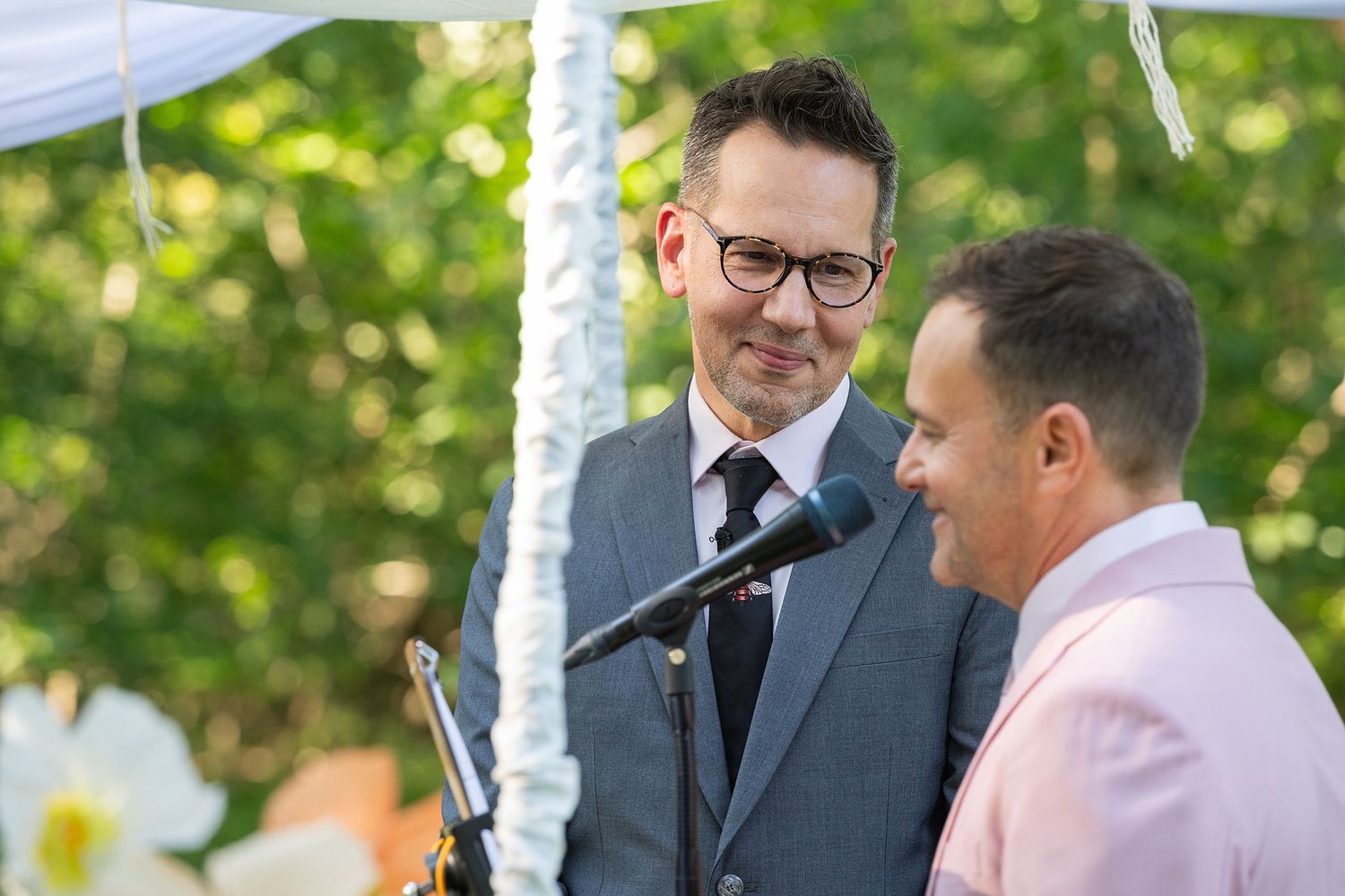 Two people share a joyful moment during an outdoor wedding ceremony in a natural garden setting.