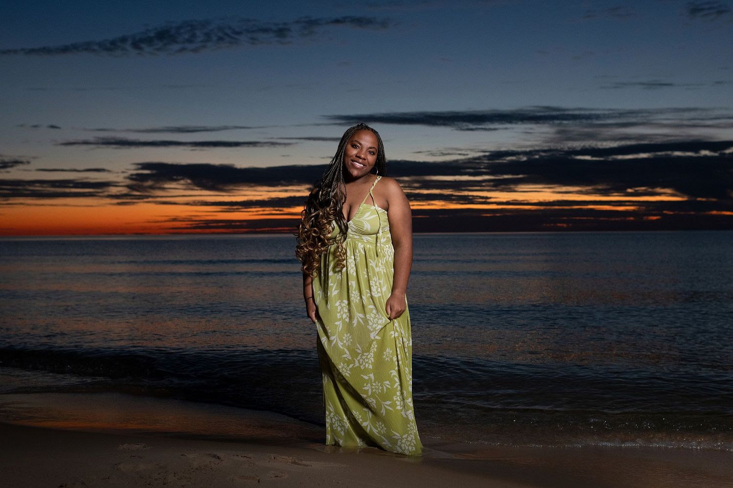 Scenic beach sunset with dark clouds and orange horizon over water.