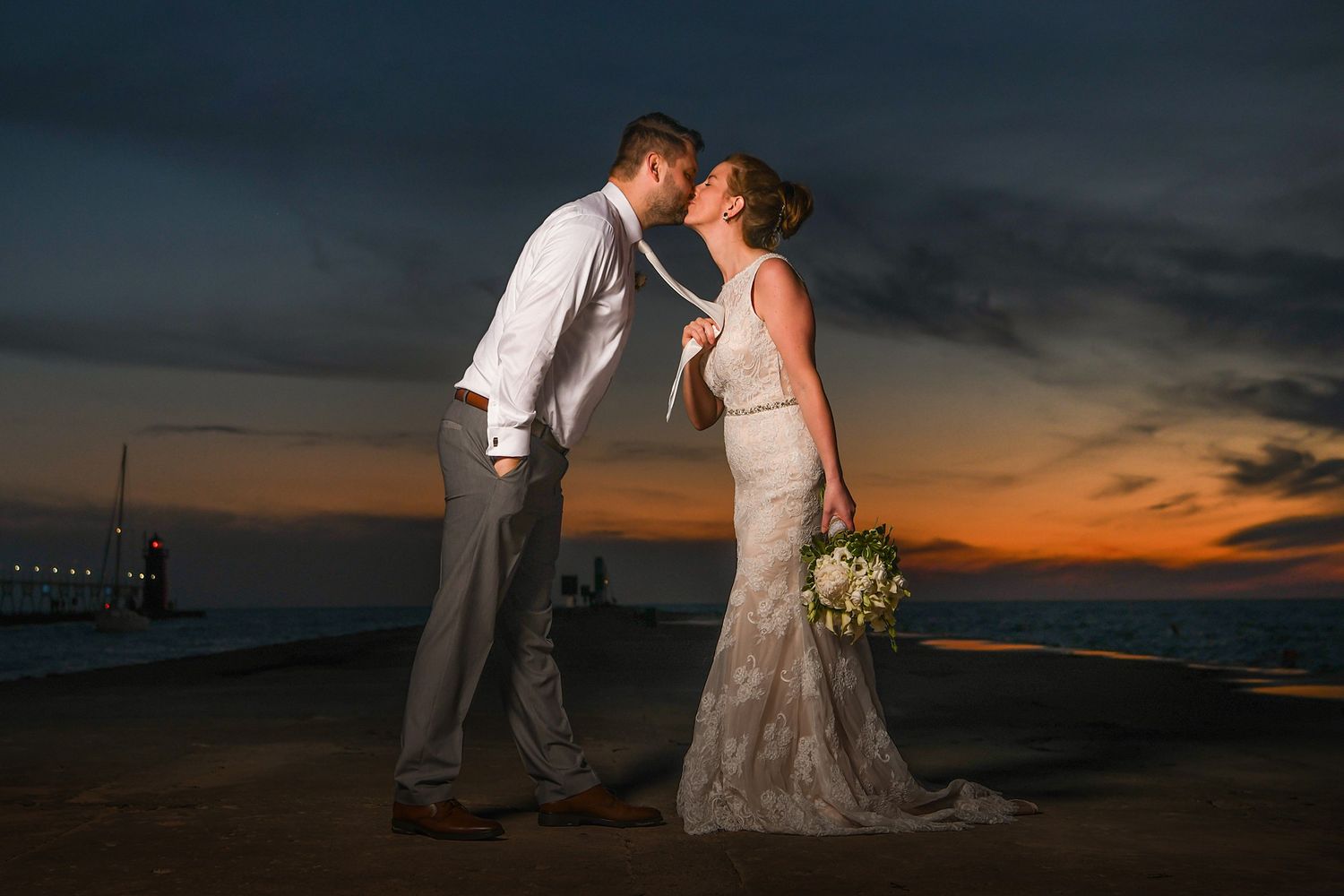 A romantic wedding couple shares an intimate moment at sunset on the beach with dramatic orange sky.