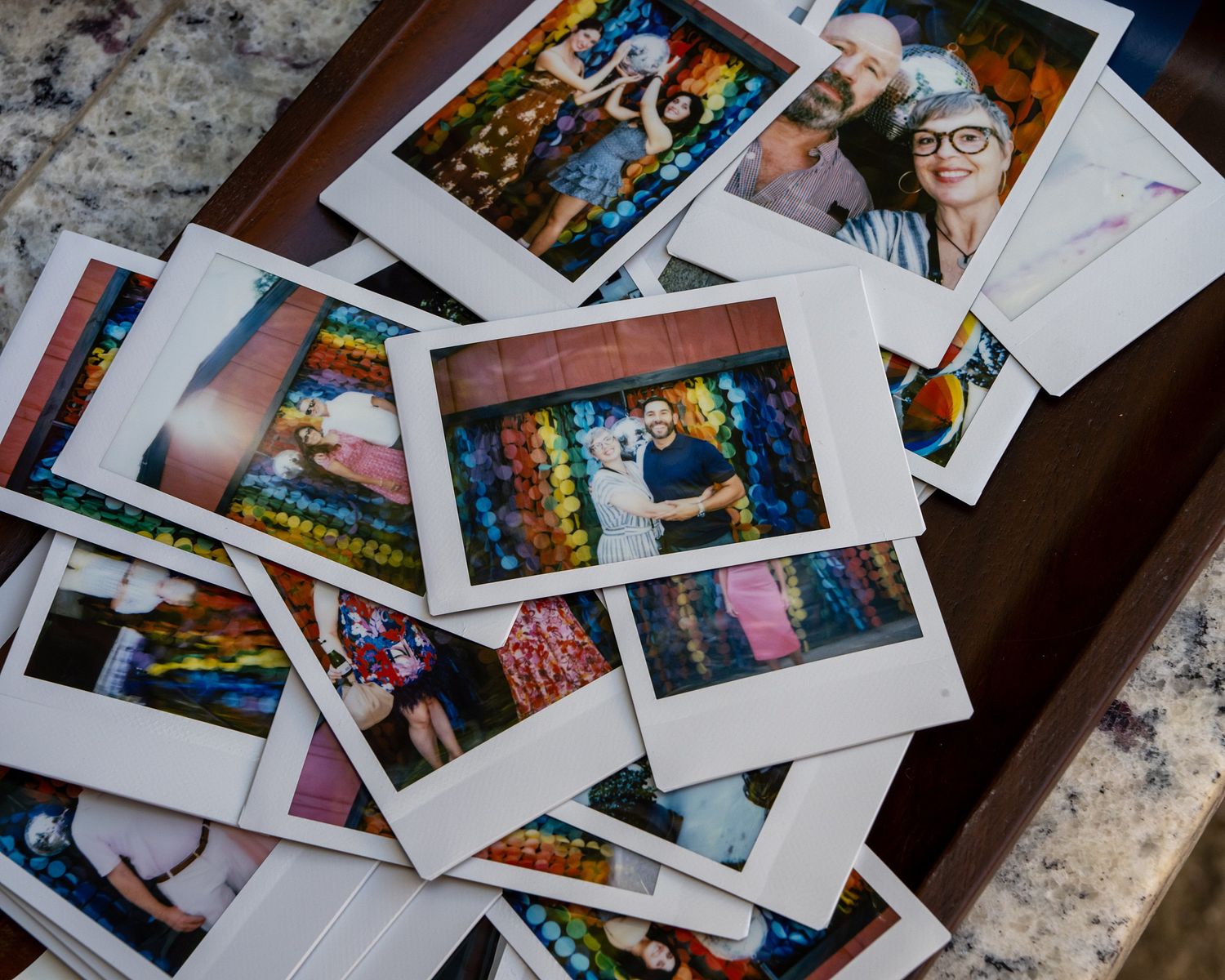 A collection of colorful polaroid photographs scattered on a marble surface showing various candid moments and memories.