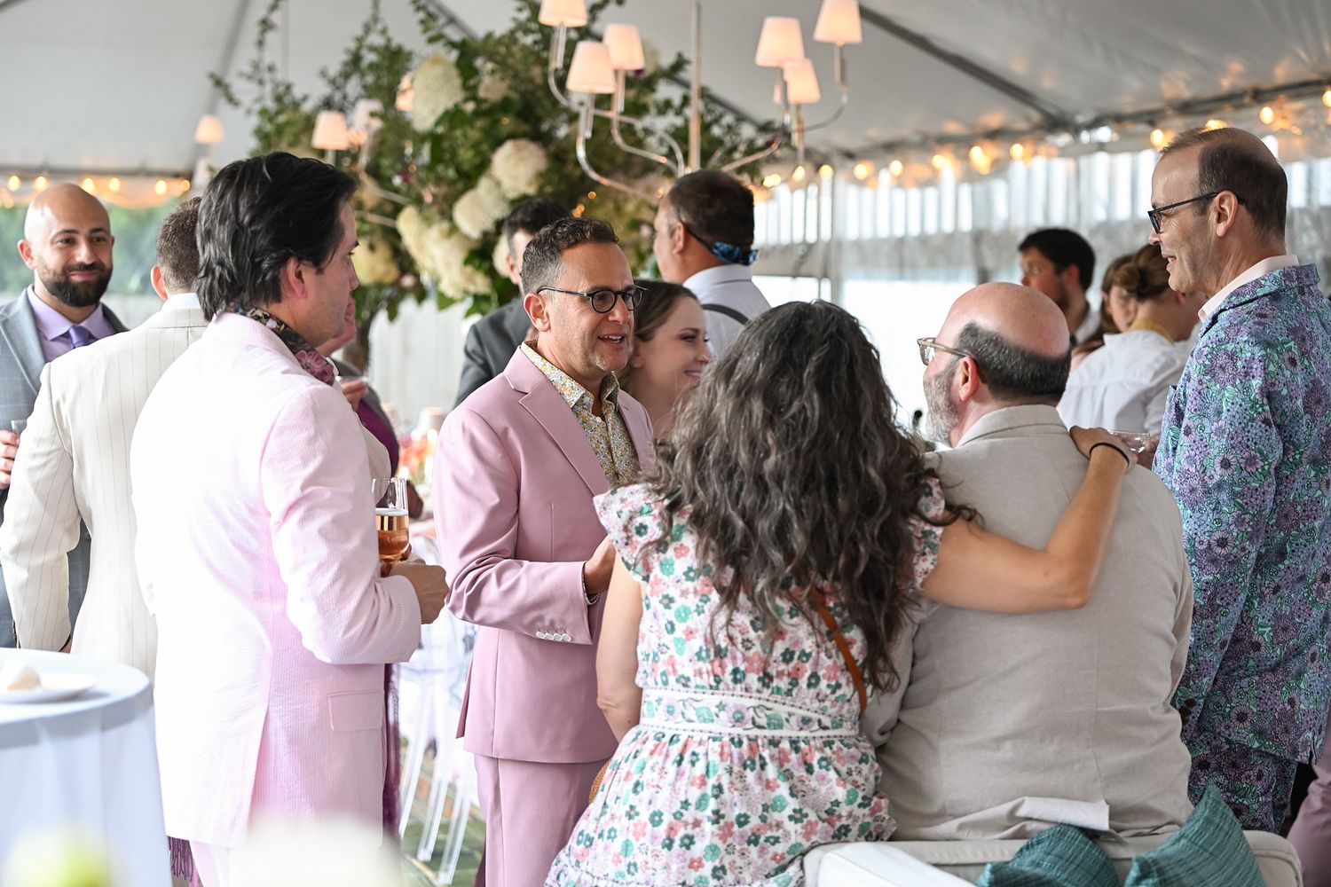 A large group of people gathered at an indoor event wearing pink and floral outfits in a bright space.