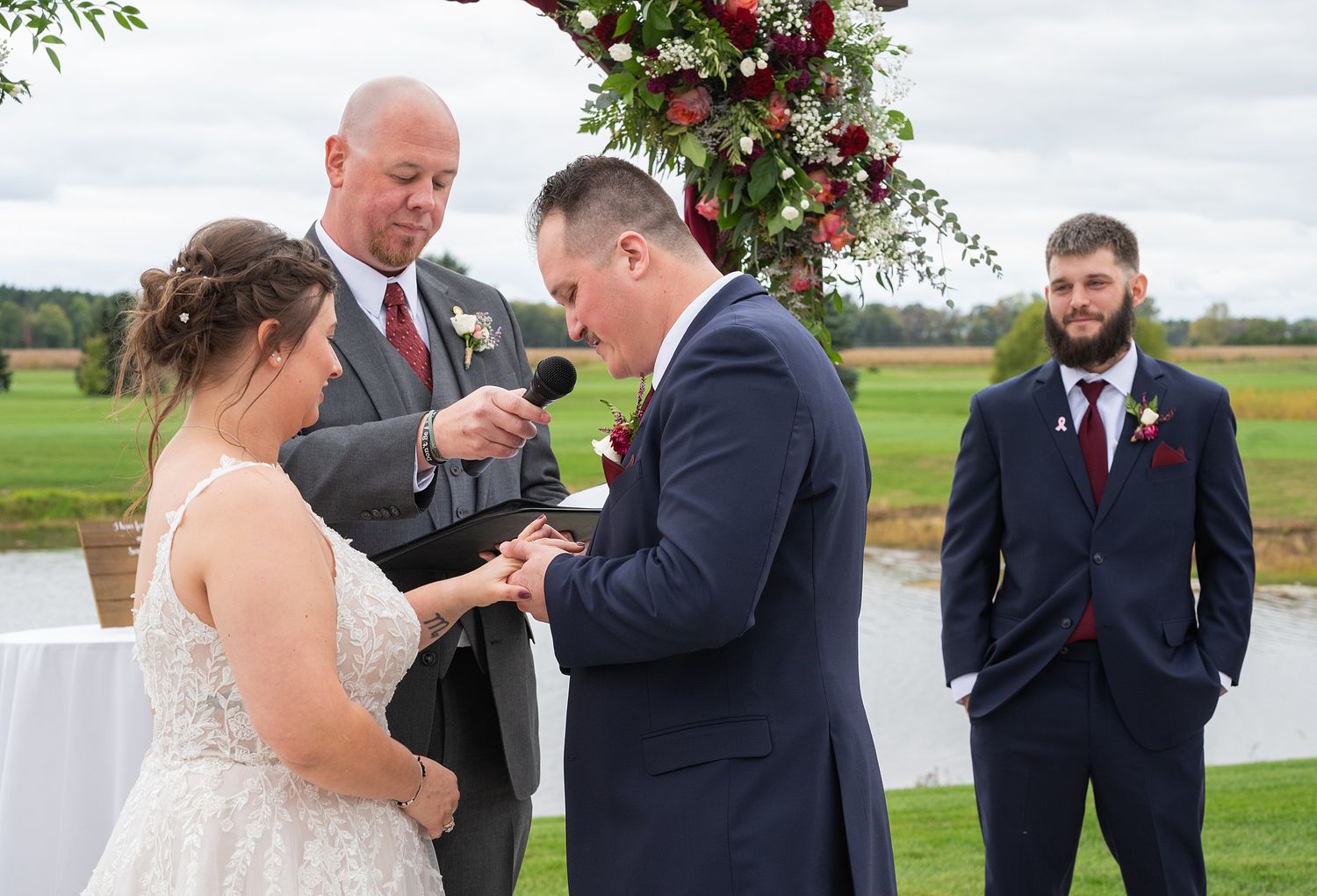 Groom places ring on brides finger during outdoor wedding ceremony.