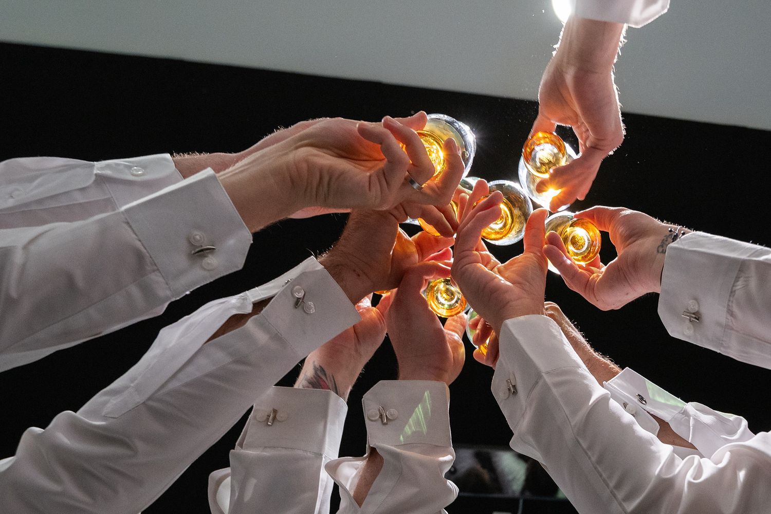 Group of people in white shirts raising glasses in a celebratory toast viewed from below.