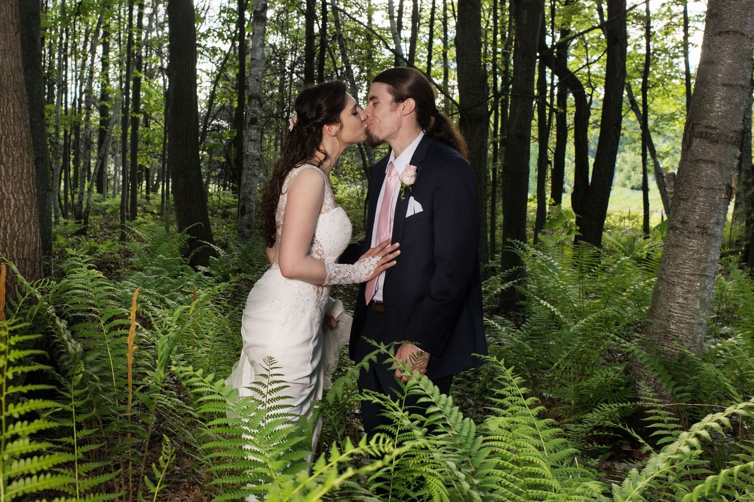 A romantic wedding moment captured in a lush forest setting surrounded by tall ferns and trees.