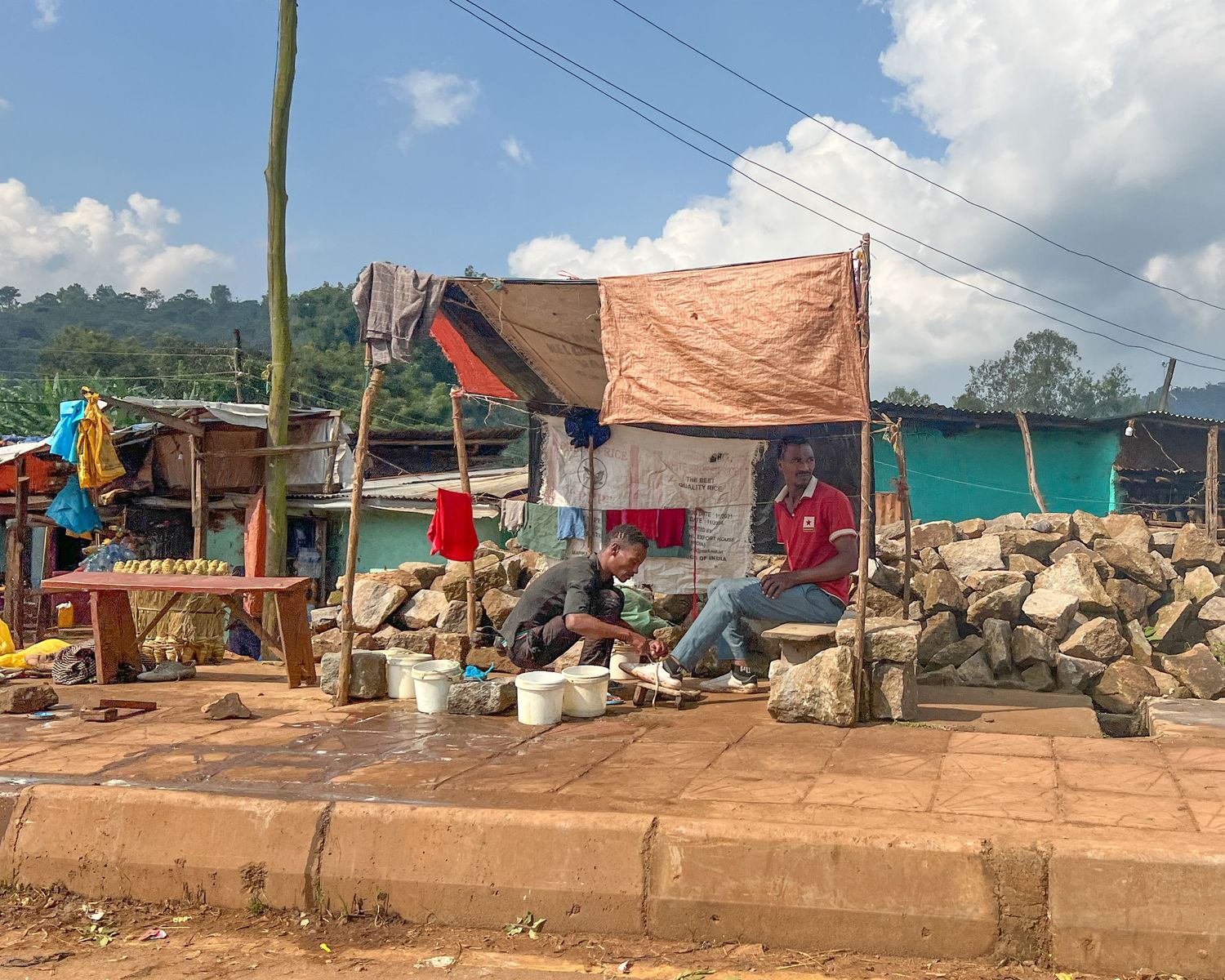Simple market stalls with tarps and temporary structures along a dirt embankment.