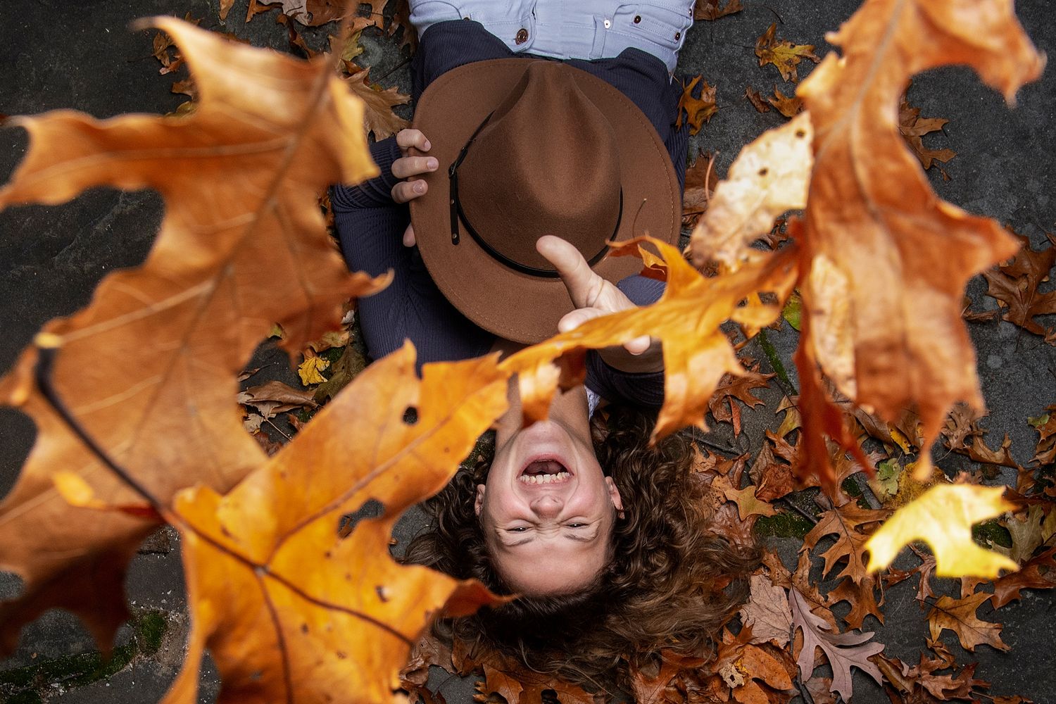 Playful autumn portrait with brown hat and swirling orange maple leaves.