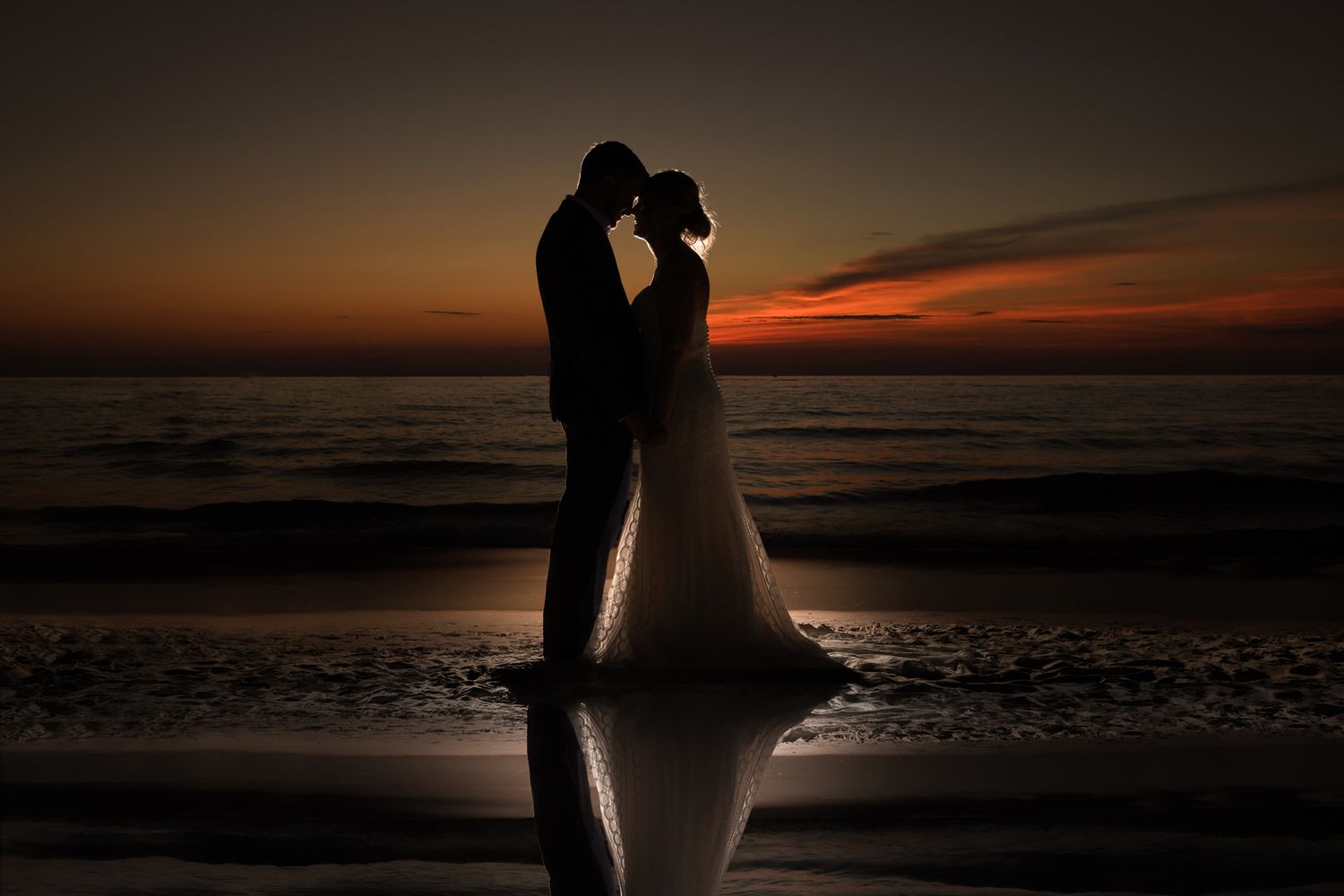 Silhouettes of couple embracing on beach during golden sunset.