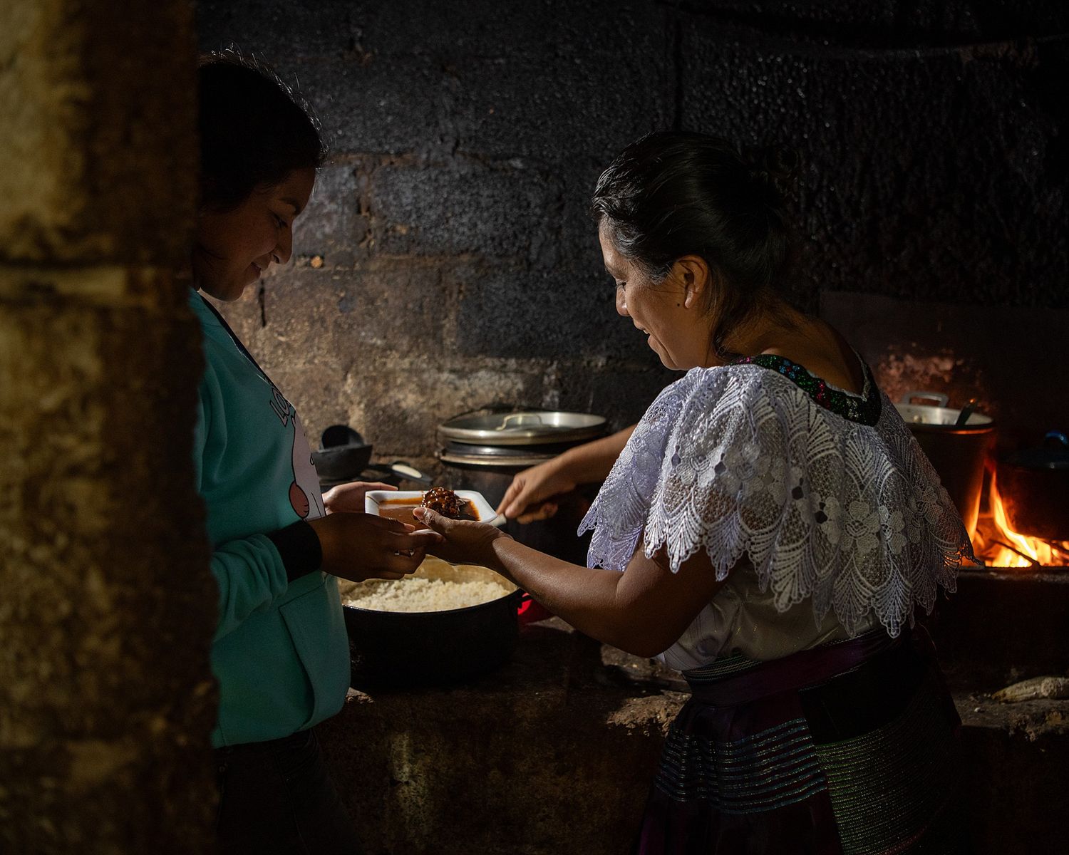A dimly lit kitchen scene showing traditional cooking methods over an open fire.