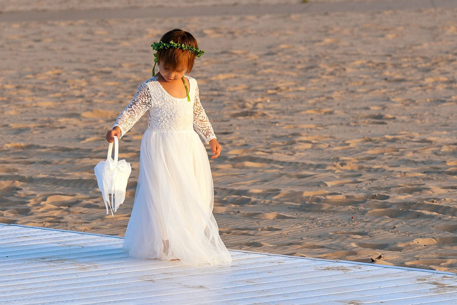 White wedding dress flowing in the breeze on a sandy beach at sunset.