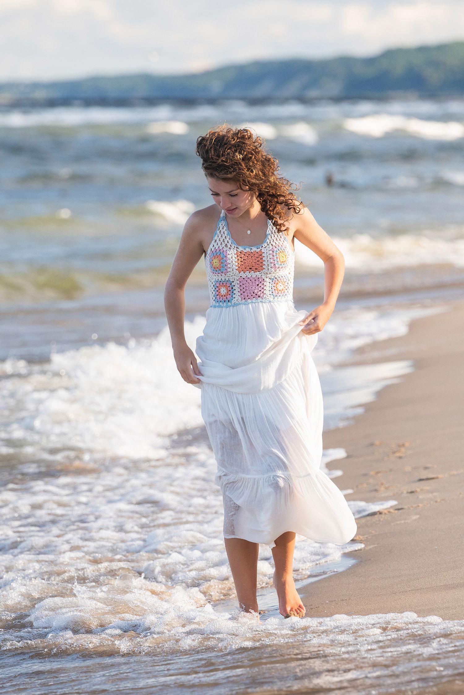 Waves lap at bare feet as a white embroidered dress flows in the ocean breeze.
