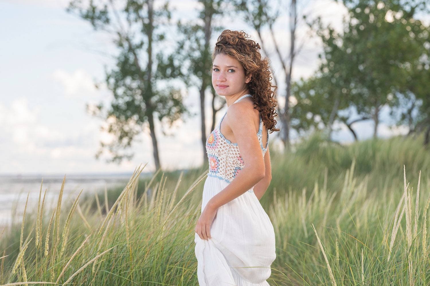 A dreamy summer scene with someone in white standing among coastal dune grass.